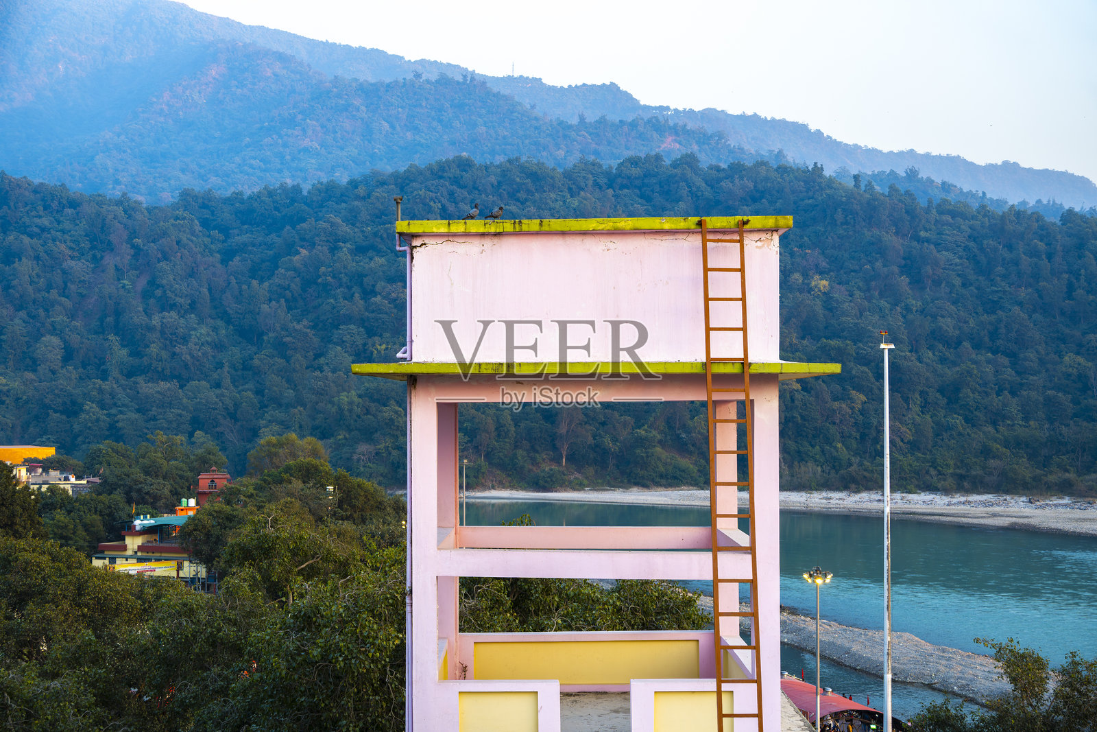 一座色彩鲜艳的水箱位于瑞诗凯诗的特里维尼河岸附近的建筑顶部,映衬着喜马拉雅山脉的希瓦利克山脊。照片摄影图片