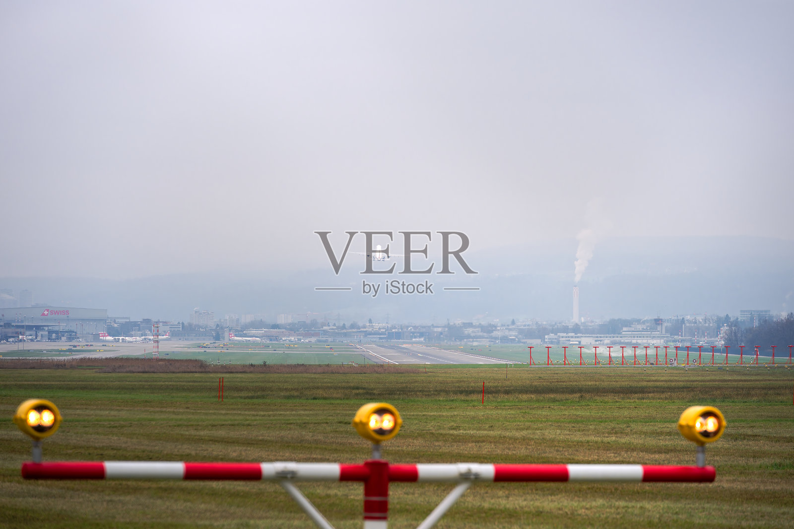 瑞士苏黎世克洛滕机场的跑道美景,航站楼灯光照耀下,客机在灰色秋日中起飞。照片摄影图片