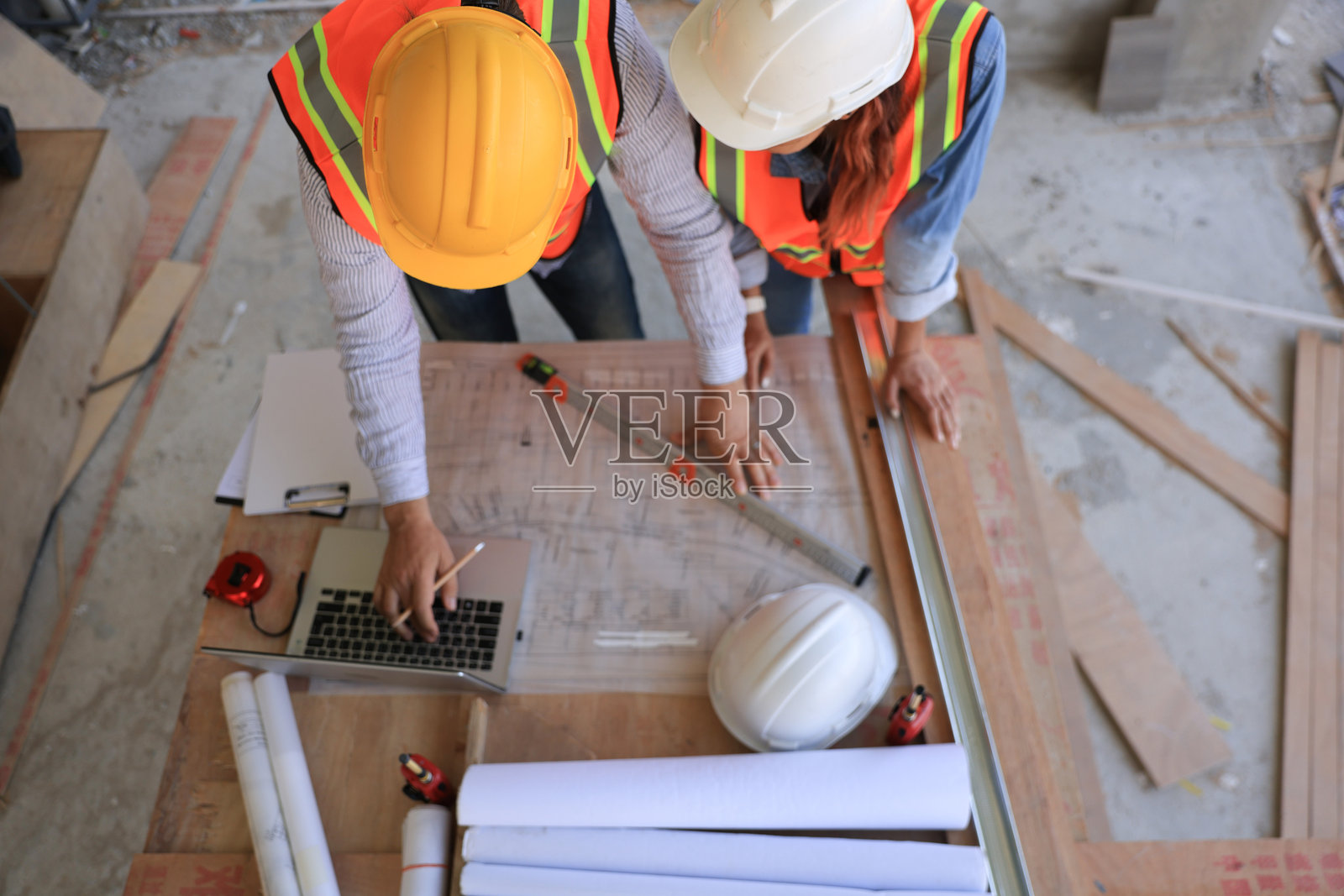 男性工程师和女性工头穿着安全背心在家居办公室施工现场一起查看蓝图图纸。照片摄影图片