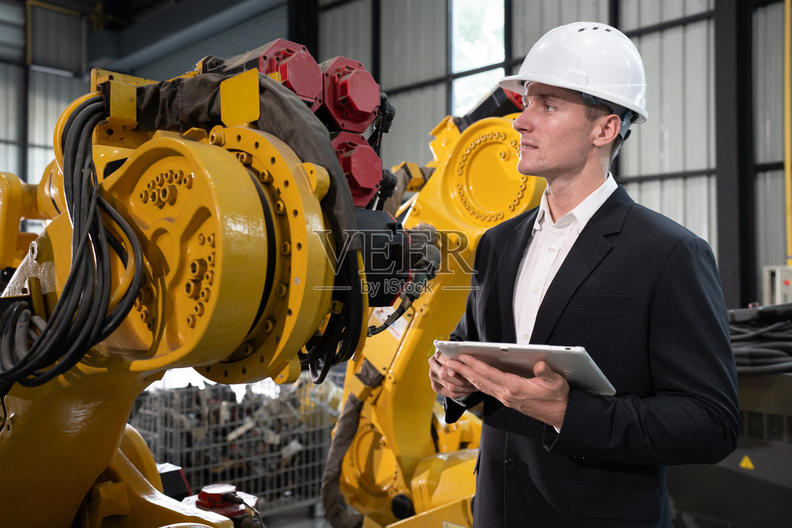 白人男性工程师或商务人士正在用数字平板检查机器人手臂的程序照片摄影图片