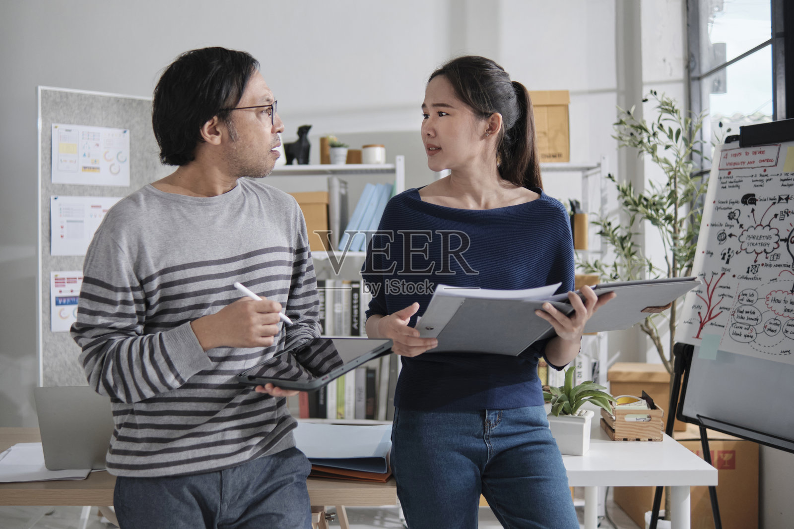 两位亚洲创业伙伴争论企业在小办公室中运作。照片摄影图片