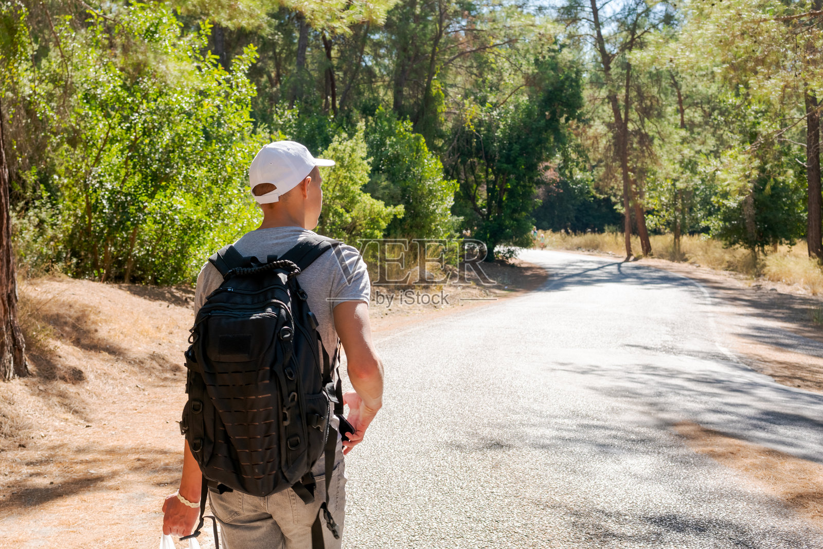 背包和帽子的男子在森林小径上徒步旅行，四周被树木和绿植环绕照片摄影图片