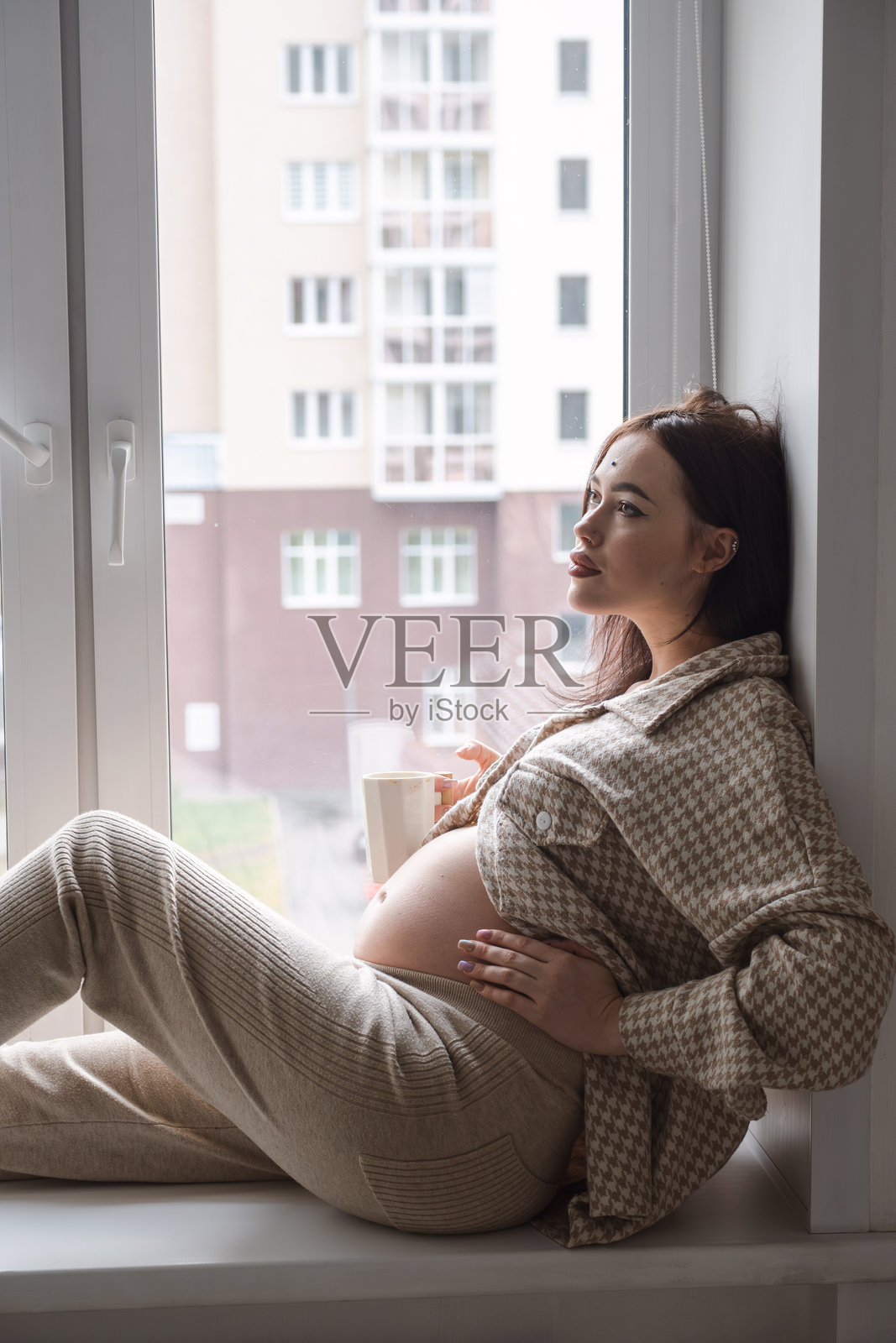 孕妇在窗边享受一杯咖啡。照片摄影图片