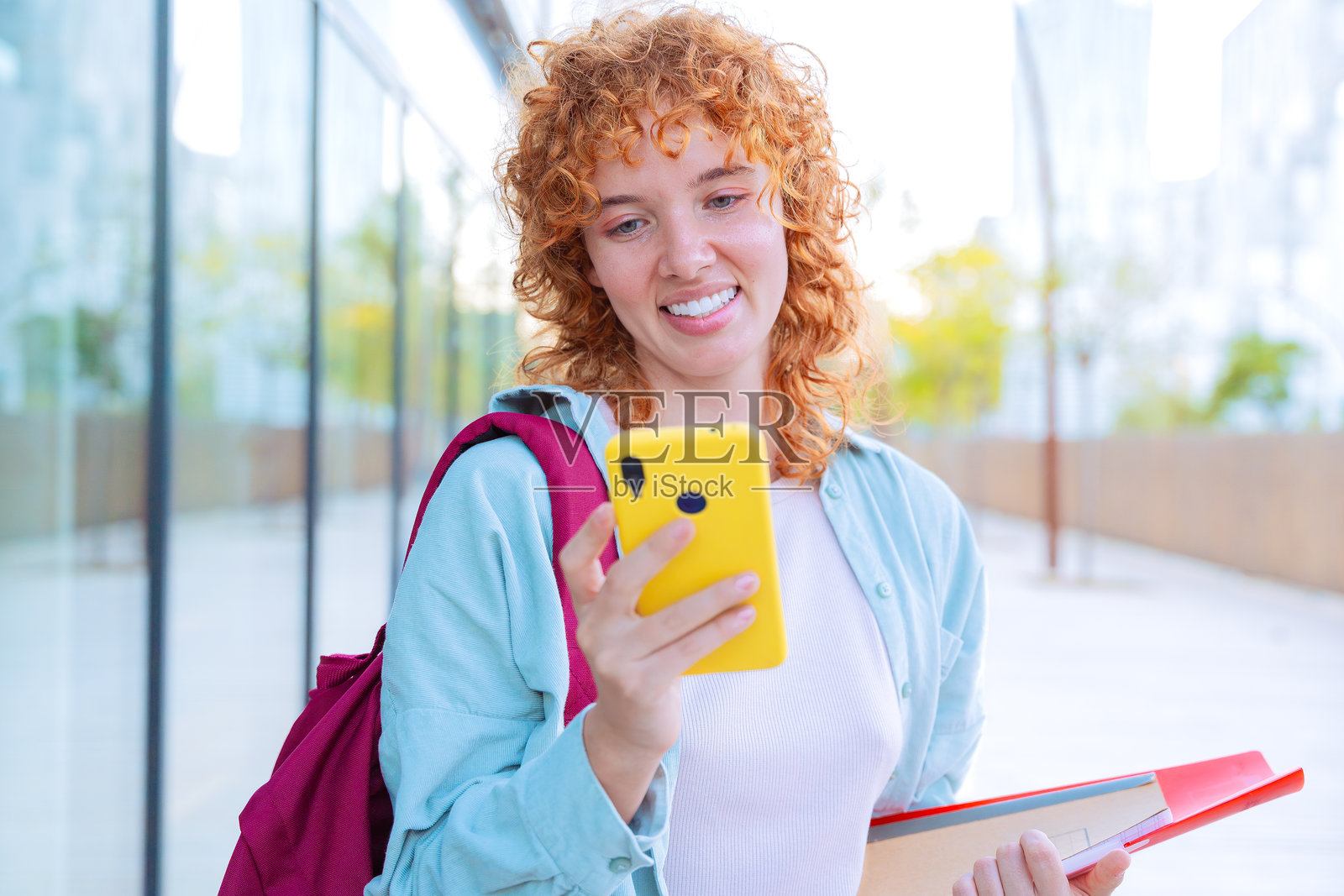 微笑的年轻女性在户外穿着休闲服装，手持智能手机和笔记本。照片摄影图片