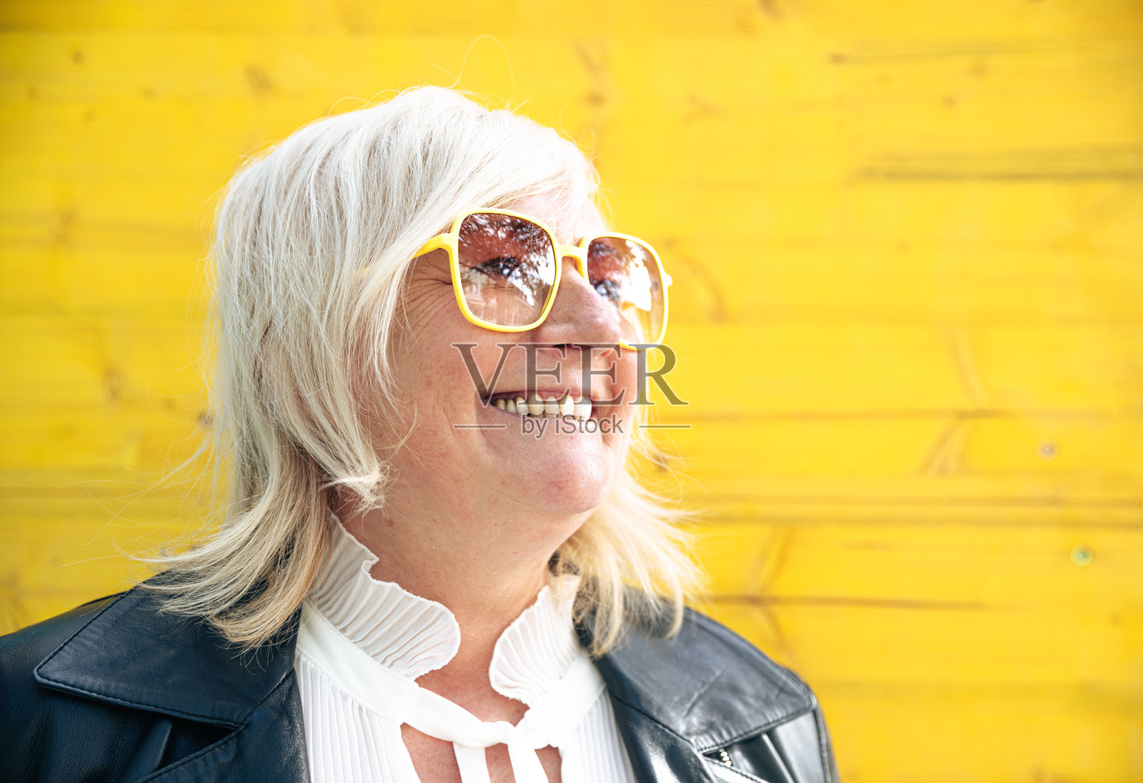微笑的老年女性戴着黄色太阳镜，背景是鲜艳的黄色。照片摄影图片