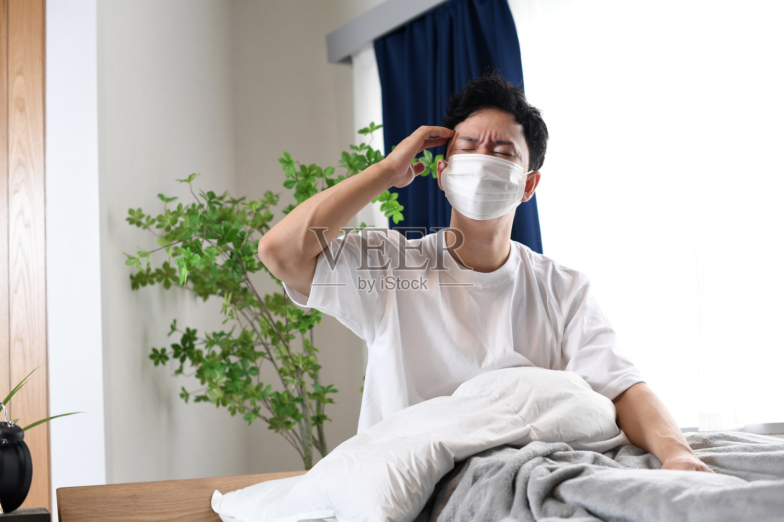年轻的亚洲男子坐在床上，痛苦地捂着头。照片摄影图片