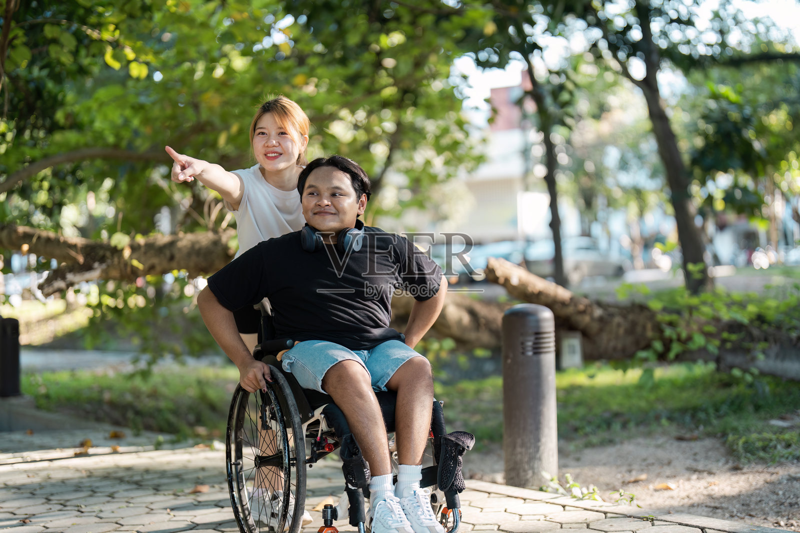 年轻女性在公园阳光明媚的日子里帮助坐轮椅的男性照片摄影图片
