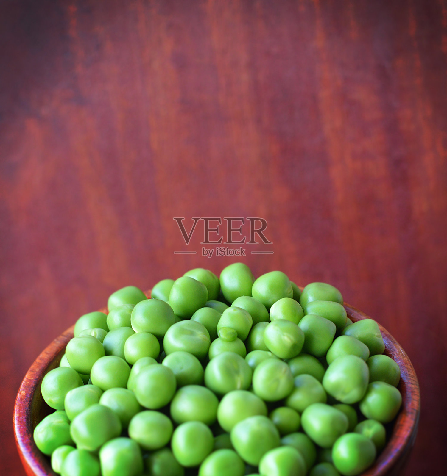 一个圆形木碗里装满了美味可口的生青豆，背景是深色木板纹理的垂直面，具有景深效果和留白空间。照片摄影图片