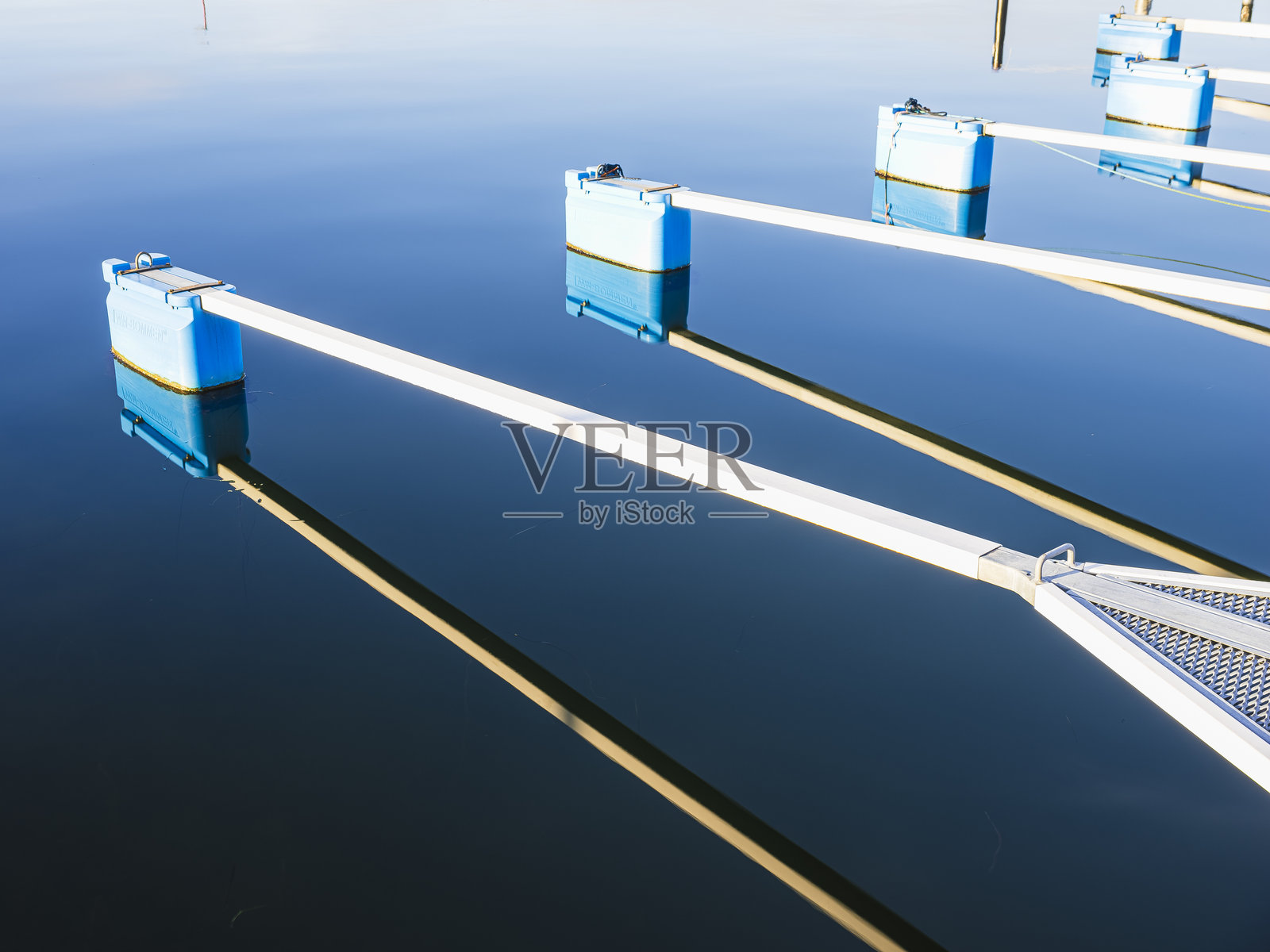 阳光明媚的日子里，宁静海边的平静水面上倒映着浮标和码头。照片摄影图片