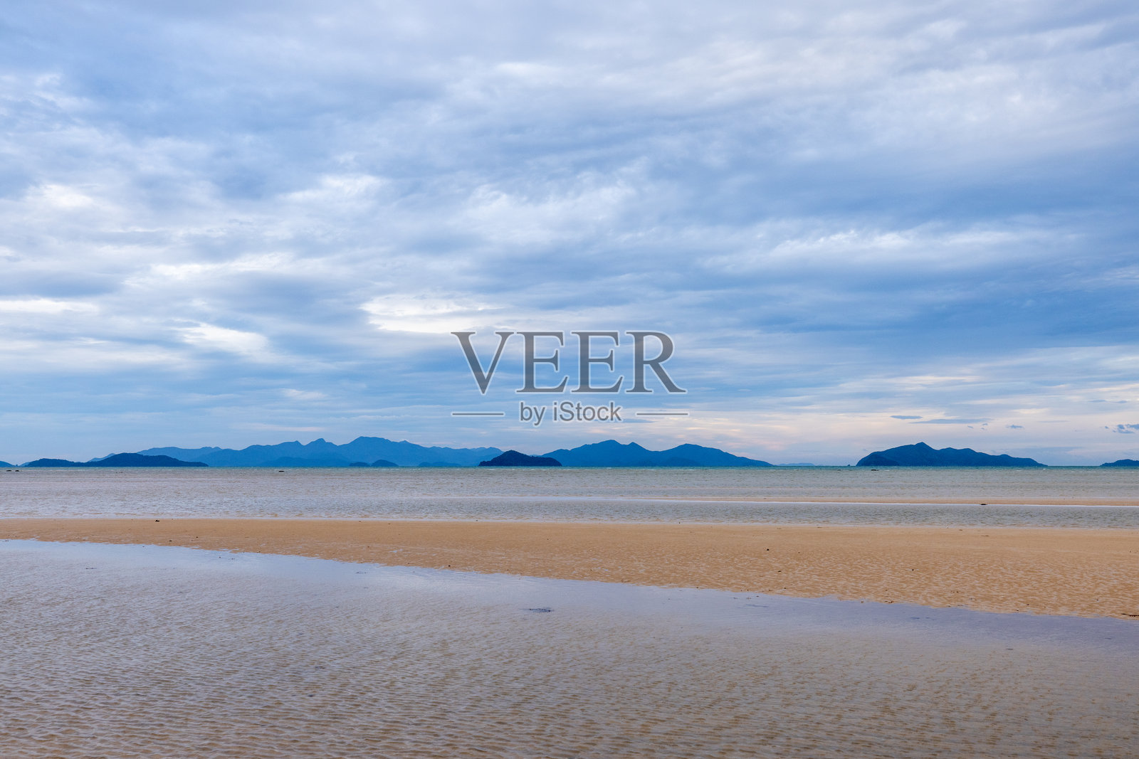 宁静的海滩与远处的岛屿在阴云密布的天空下照片摄影图片