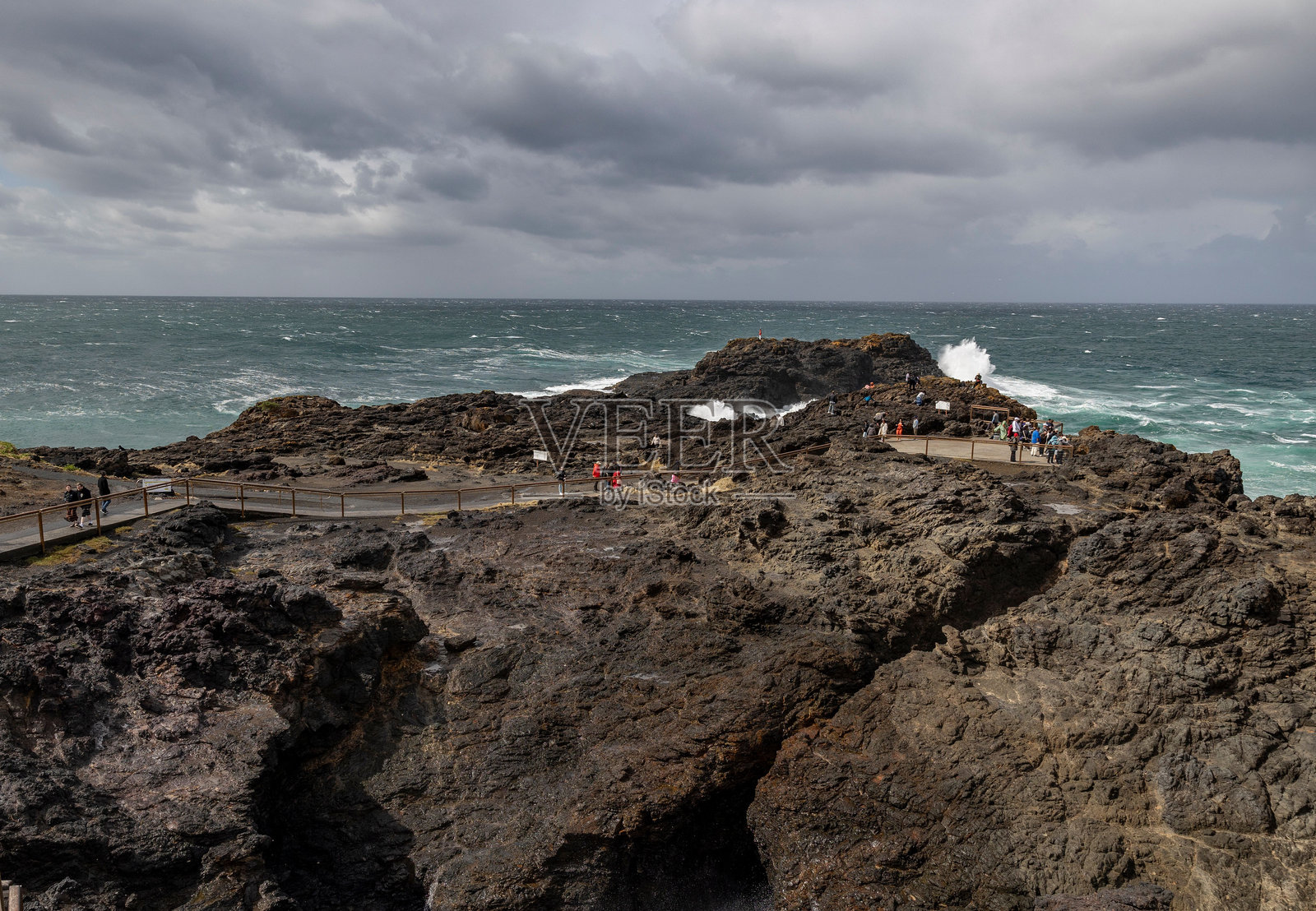 游客在岩石海岸上欣赏壮观的海浪。照片摄影图片