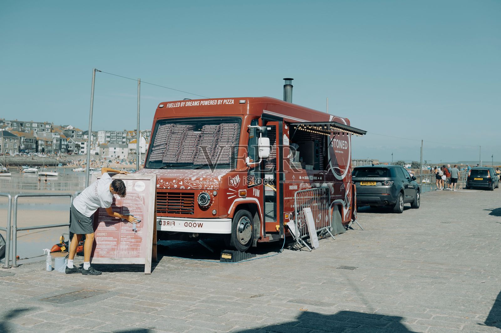 海边色彩鲜艳的餐车，一人正在清洁菜单板照片摄影图片