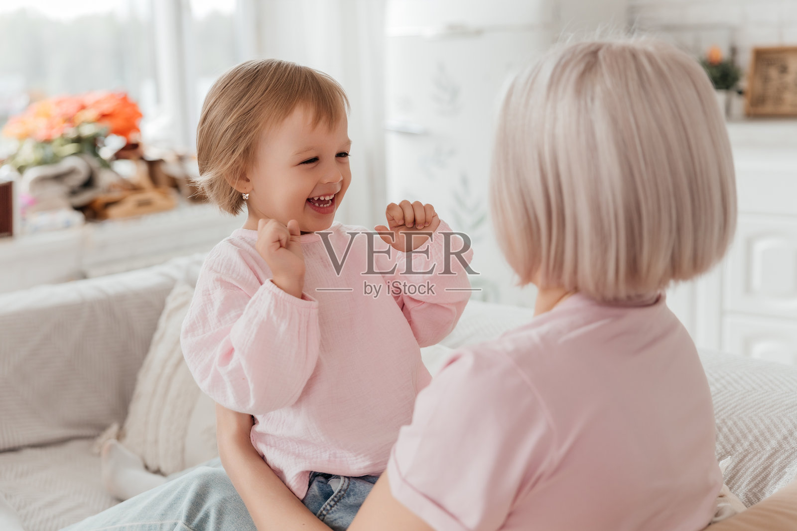 一个三岁的小女孩在明亮的客厅里和她的妈妈一起在沙发上玩耍。照片摄影图片