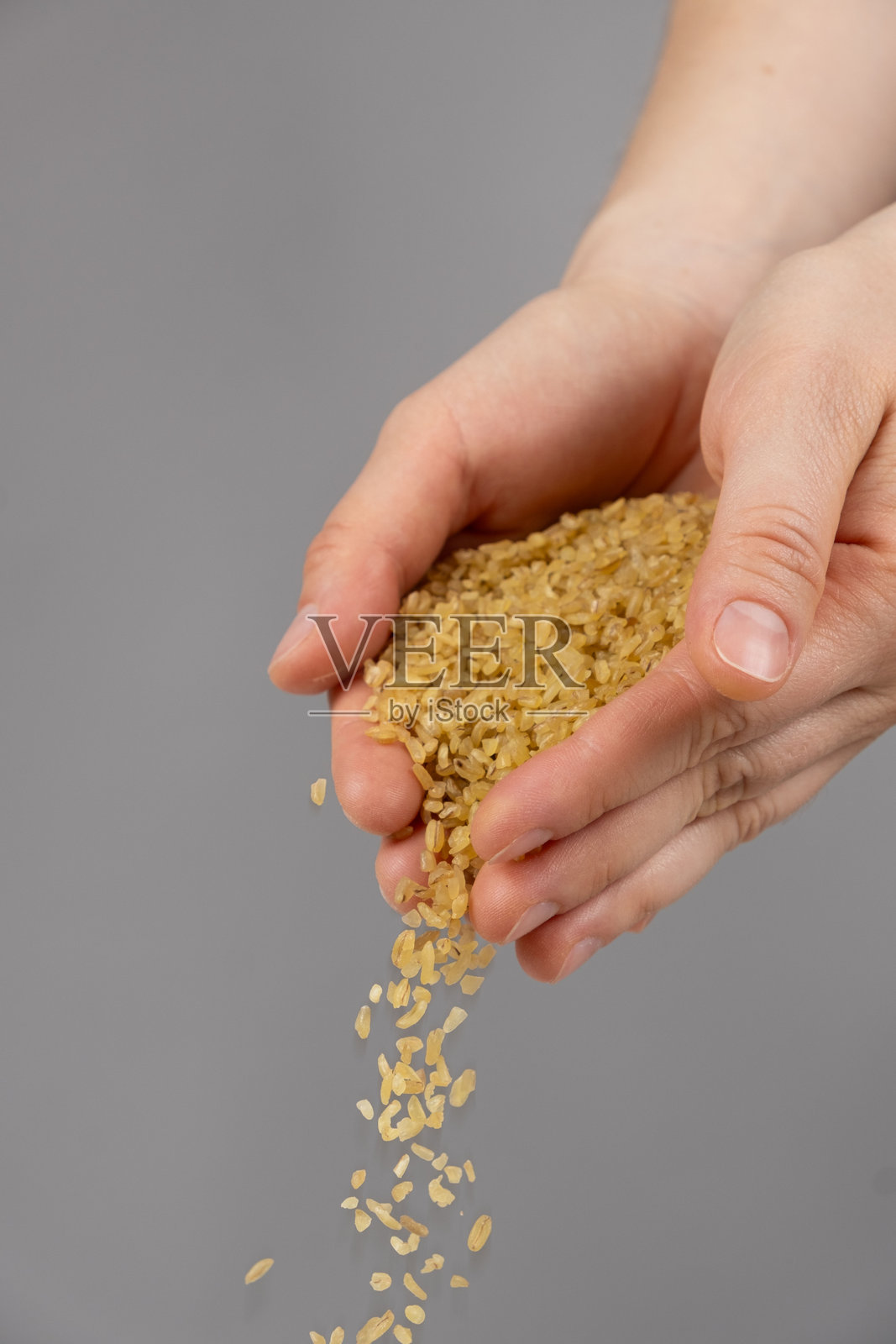 手将生的未煮熟的粗麦粉倒在灰色背景上。照片摄影图片