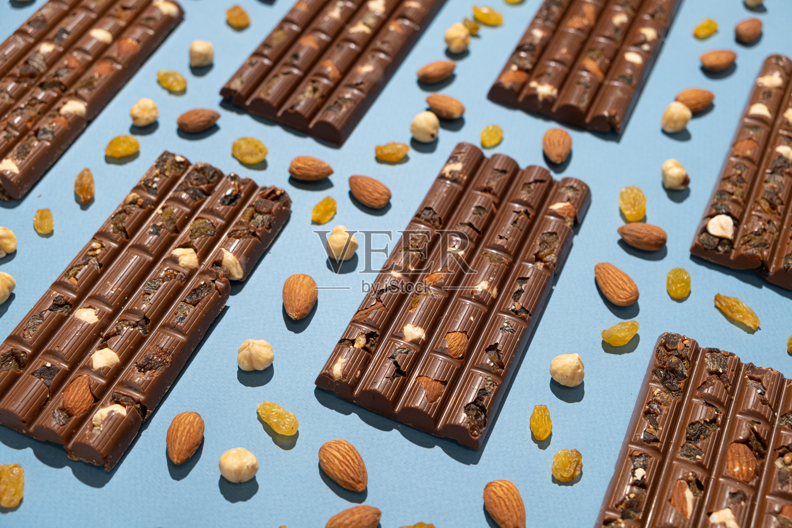 蓝色背景上散落着坚果和葡萄干的坚果巧克力棒。照片摄影图片