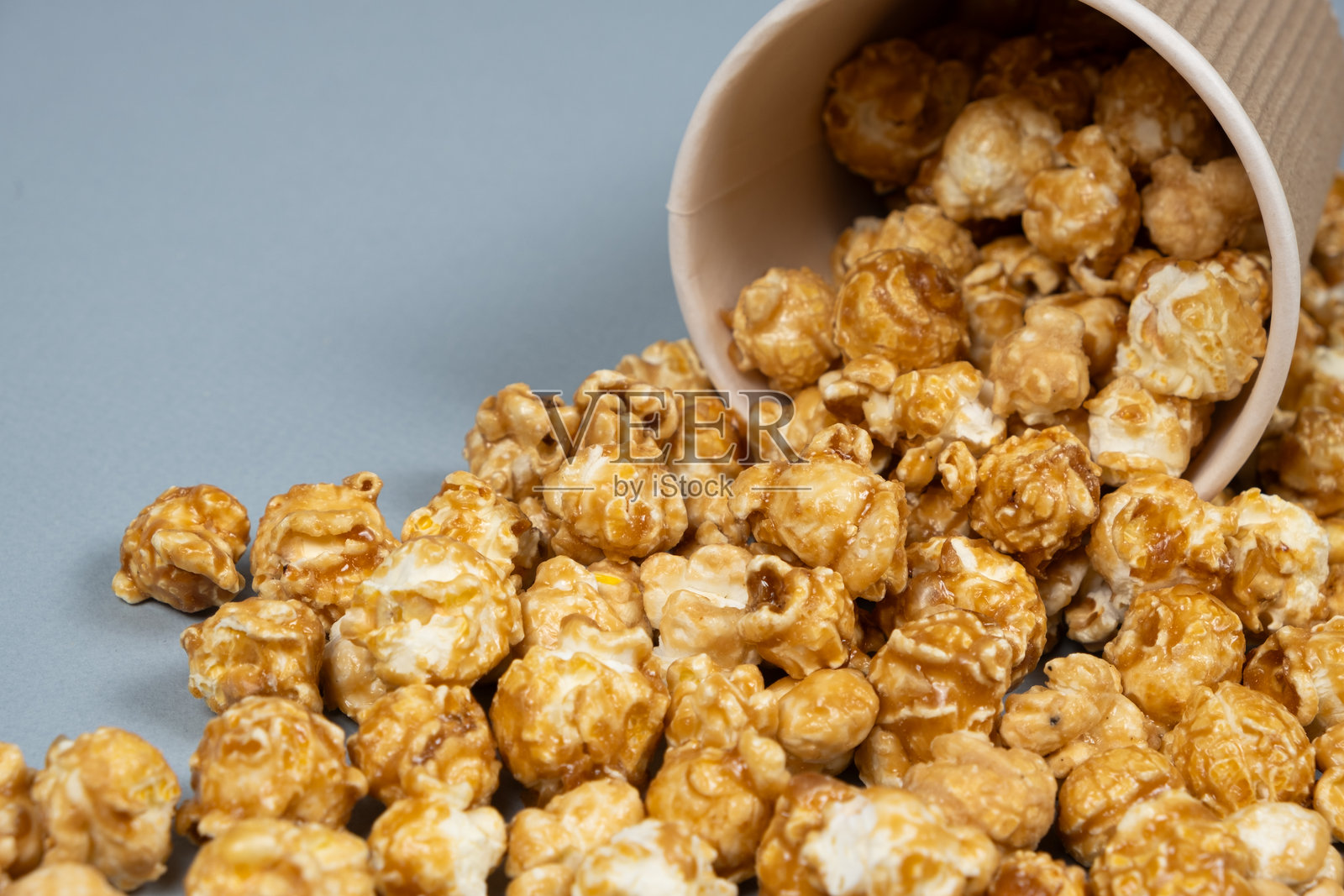 甜美的焦糖爆米花洒落在玻璃外。照片摄影图片