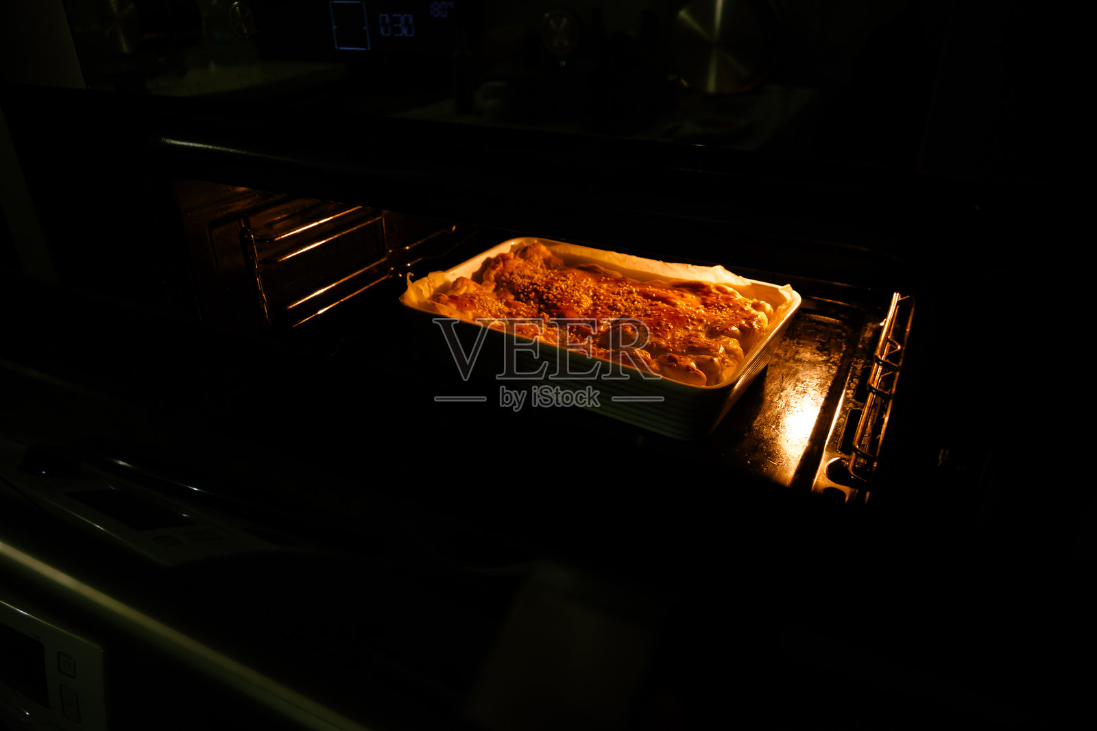 金黄色的派，酥脆的外壳上撒满了芝麻，正在温暖的烤箱中烘烤。家常糕点的概念，温馨的家庭烘焙。照片摄影图片