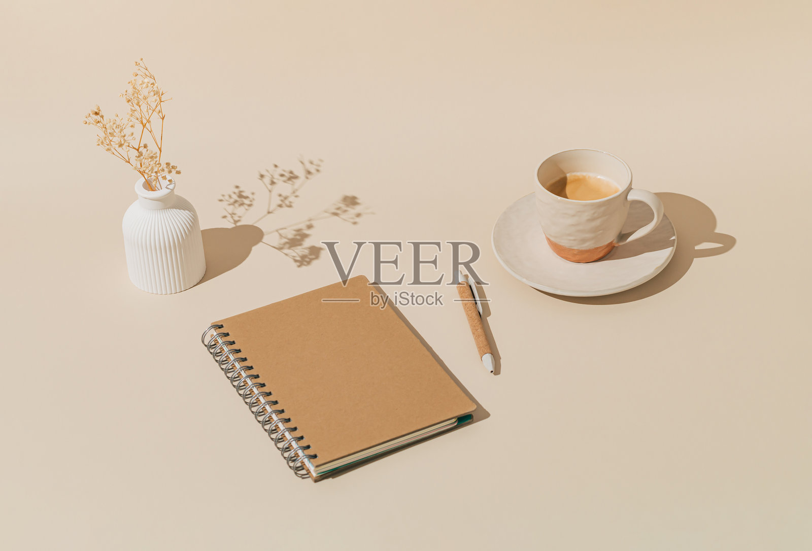 时尚的布局，包含咖啡杯、白色花瓶（内有干花）、笔记本和钢笔，背景为柔和的奶油色。极简创意概念。照片摄影图片
