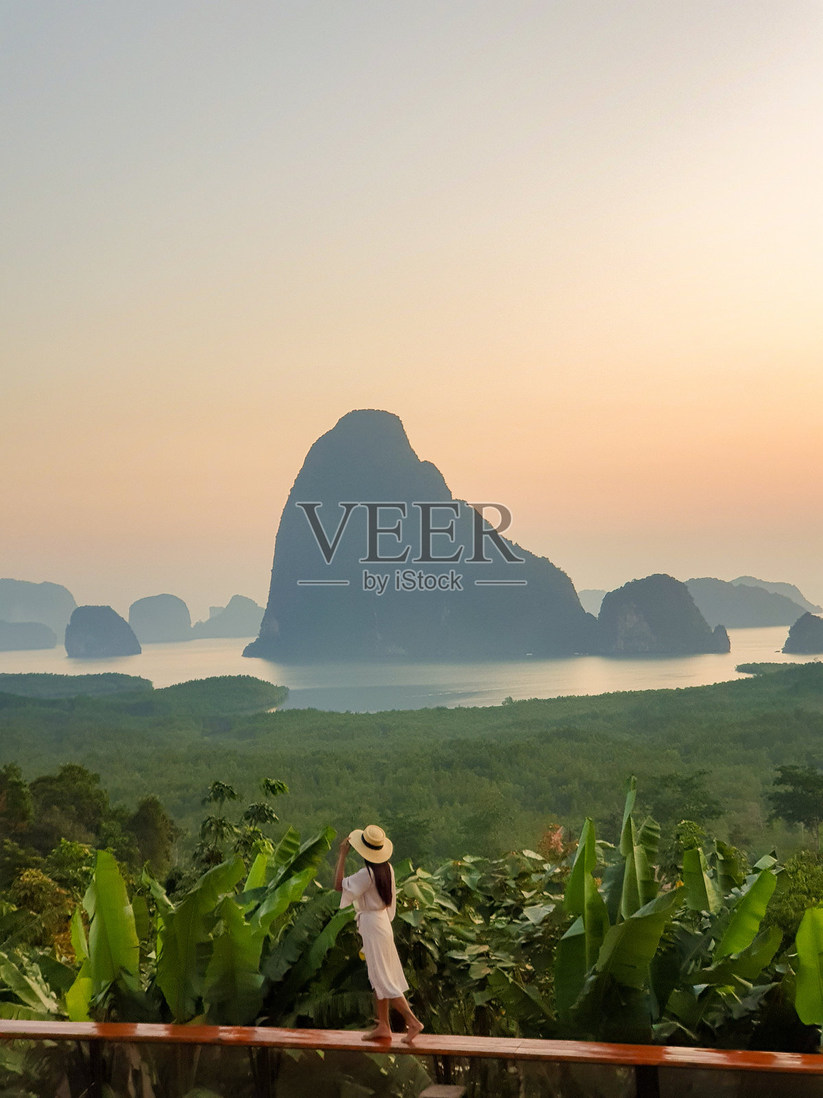 一位女性在泰国攀牙湾欣赏宁静的日落美景，远处是山脉和海洋。照片摄影图片