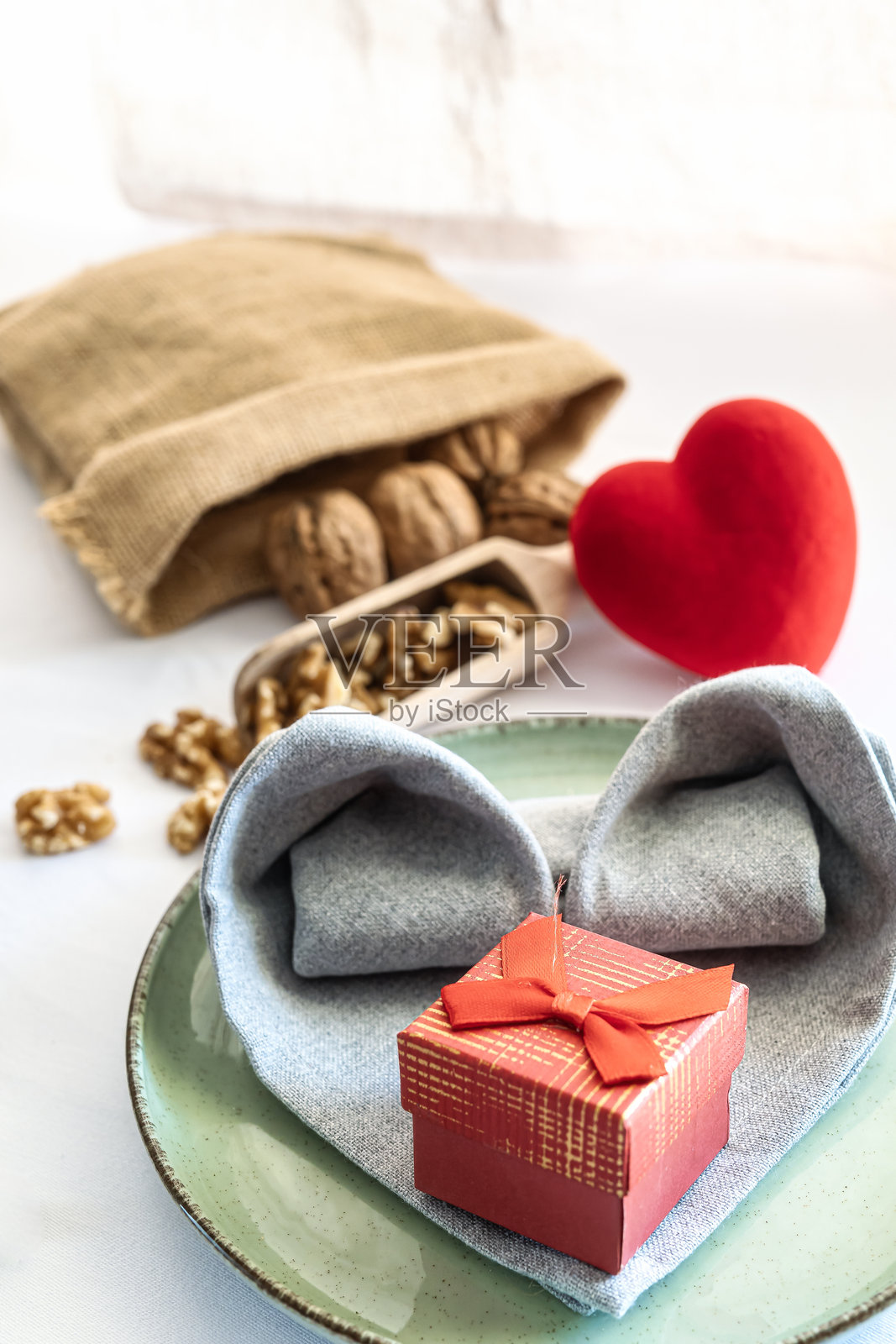 盘子上放着心形餐巾的特写，旁边有一份礼物，桌子布置得浪漫，适合情人节和爱的主题。照片摄影图片