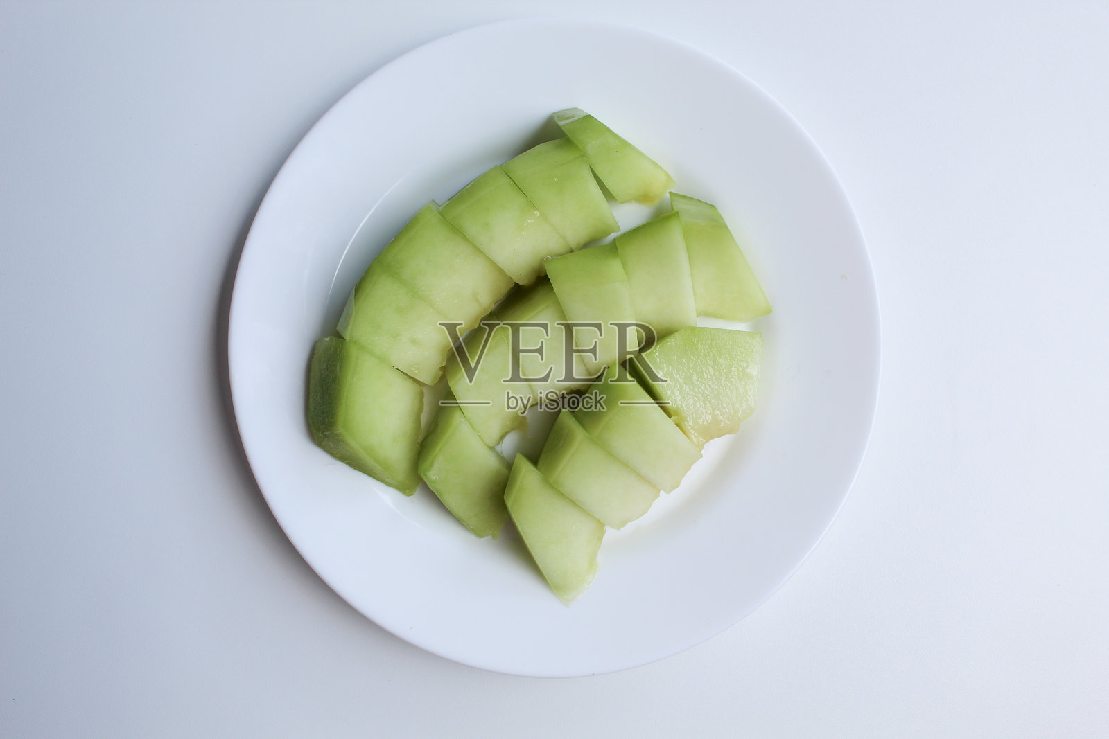 白色盘子上的小块绿色哈密瓜或甜瓜，孤立在白色背景上，俯视图或平视图照片摄影图片