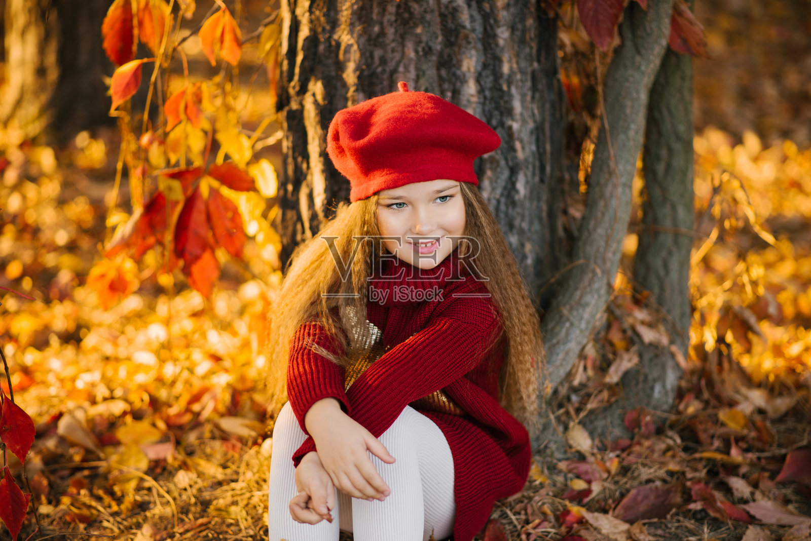快乐的白人女孩坐在公园的树旁，享受阳光明媚的日子照片摄影图片