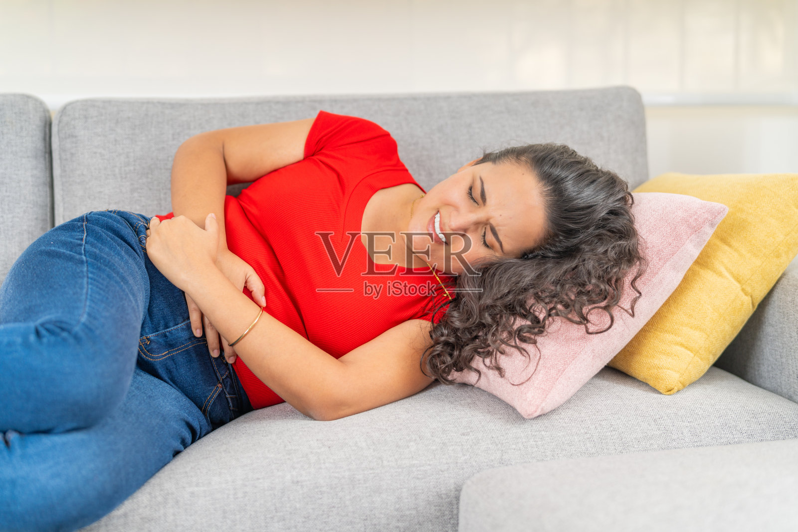 年轻女性躺在沙发上，感到剧烈的腹痛照片摄影图片