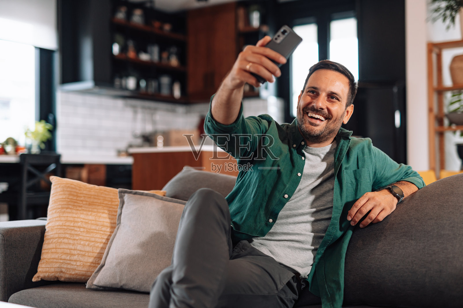 快乐的男人坐在家里的沙发上用手机自拍照片摄影图片