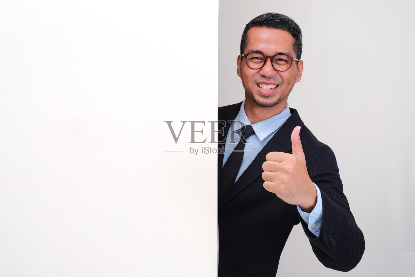 一位商人从墙后探出头来，面带笑容竖起大拇指。照片摄影图片