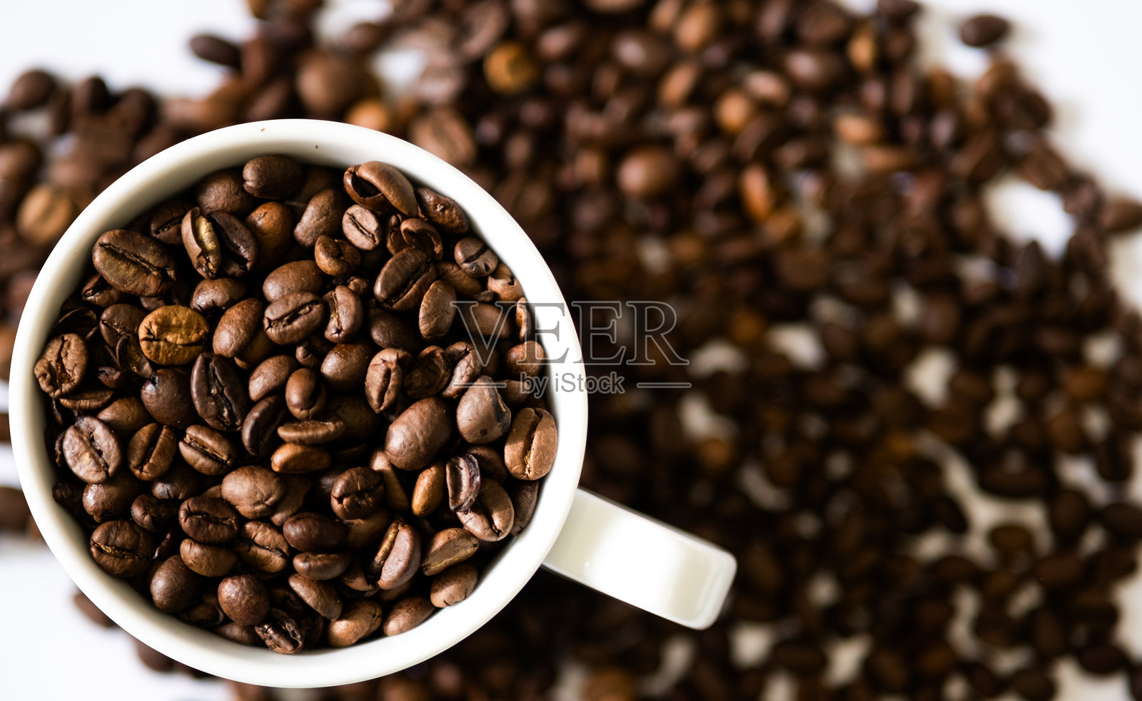 白色咖啡杯中的一堆咖啡豆，背景是咖啡豆。照片摄影图片