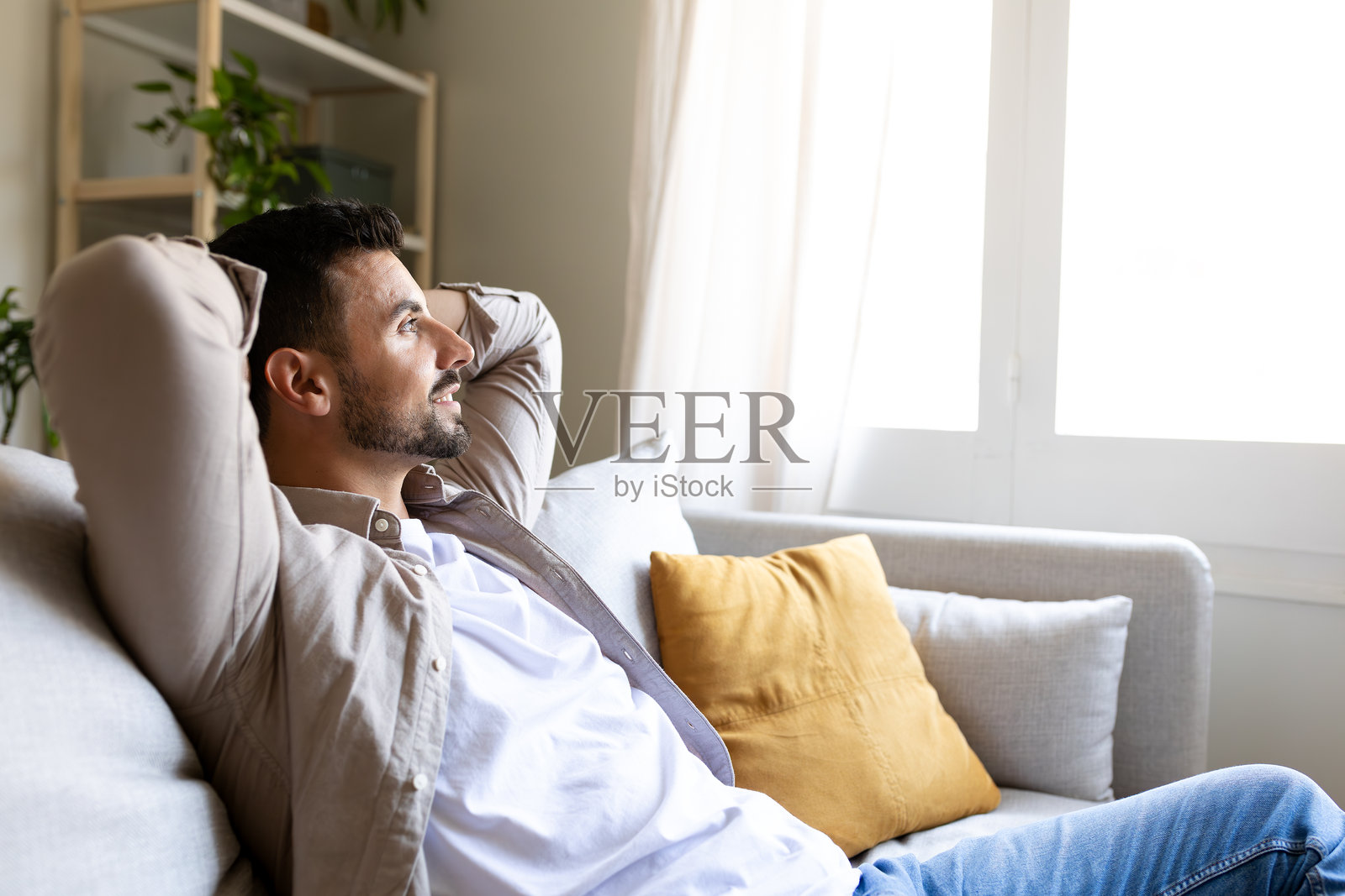 侧面视角的放松男人坐在沙发上，双手放在头后，凝视窗外，神情沉思。留白空间。照片摄影图片