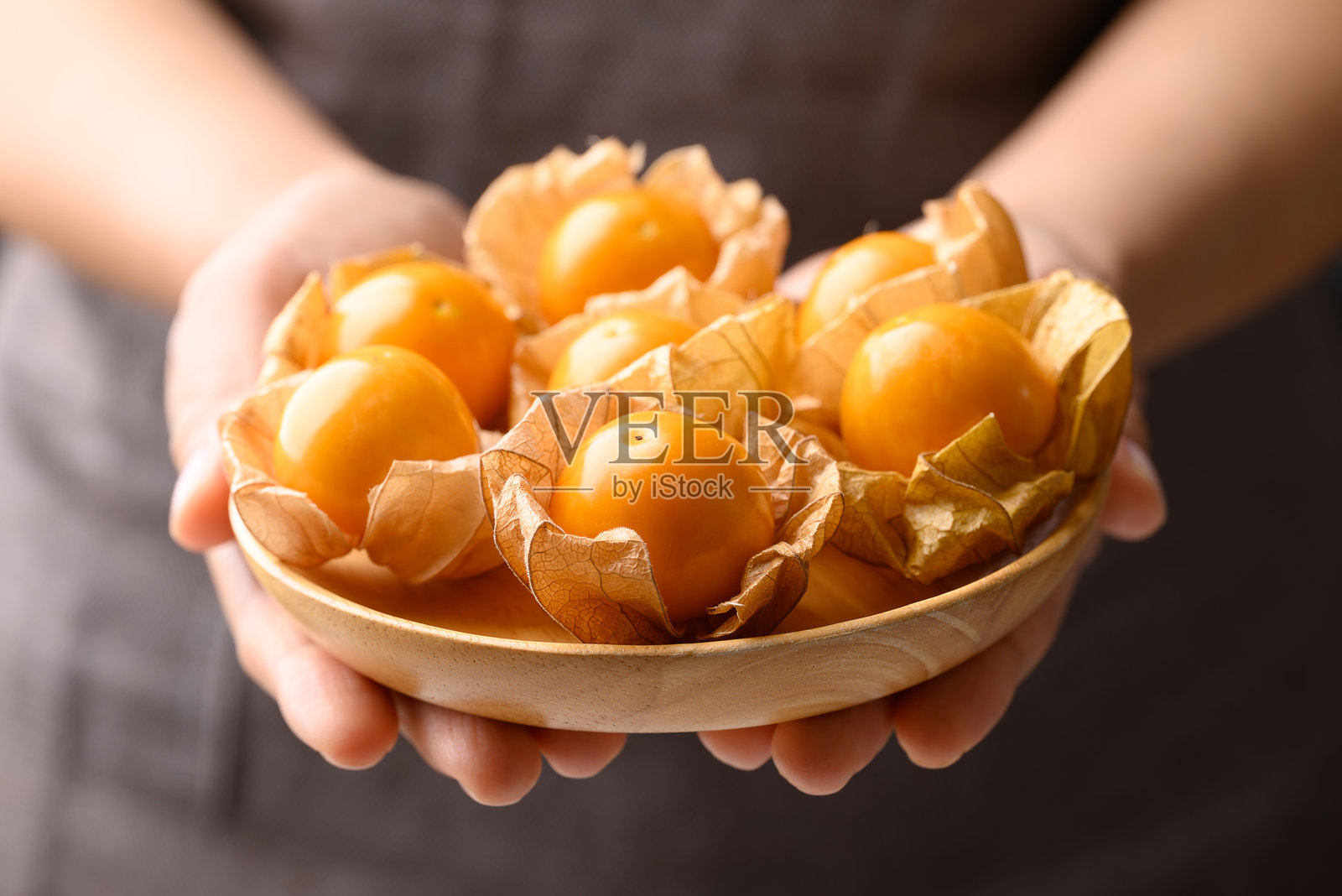 手中捧着碗装的灯笼果或金果（Physalis peruviana），健康的水果照片摄影图片