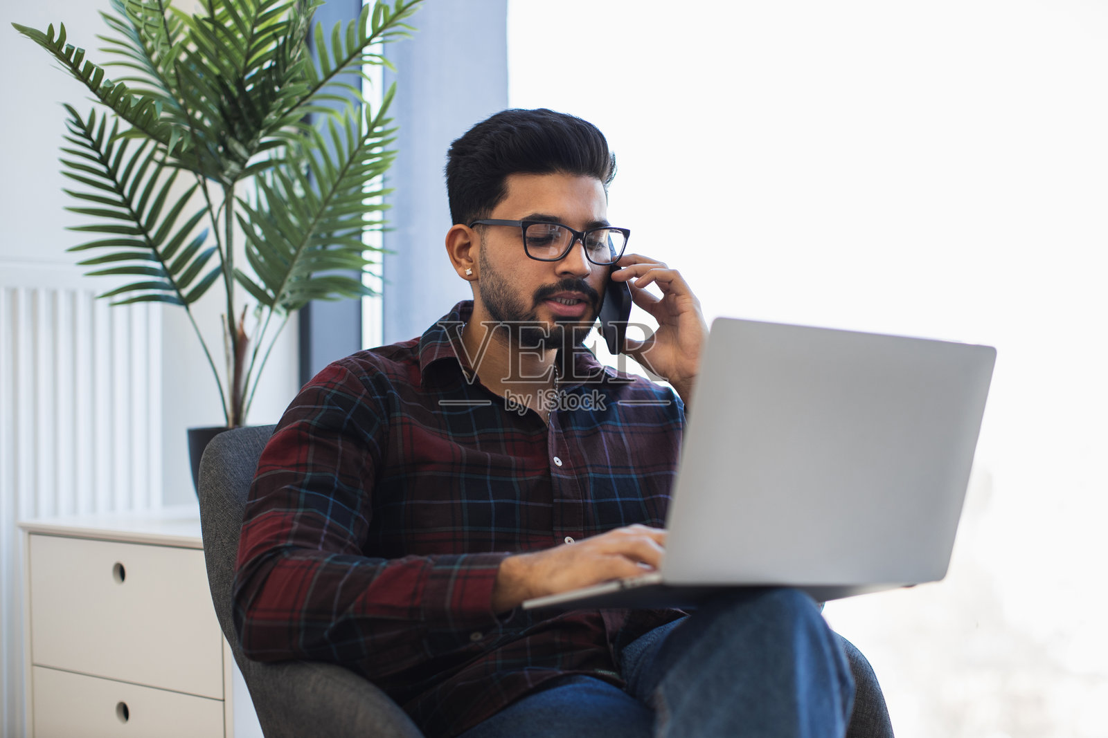 印度男子在家办公室使用笔记本电脑和手机远程工作照片摄影图片