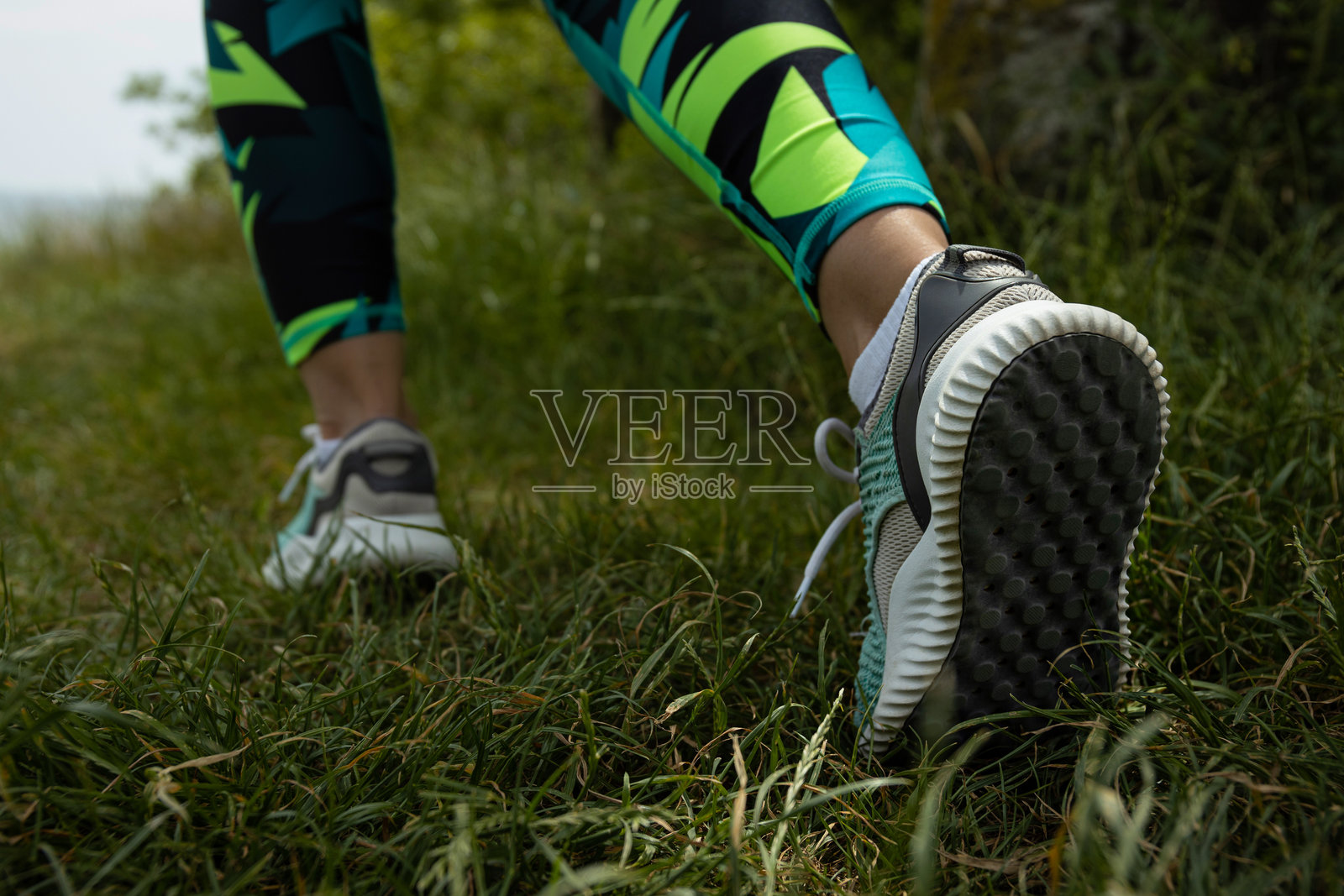 穿着运动鞋的女性在草地上行走，特写镜头展示她的运动腿部。照片摄影图片