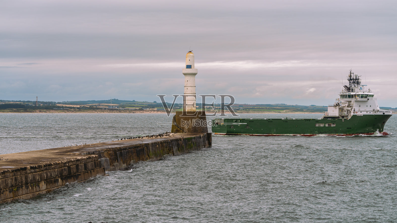 一艘船离开港口,经过苏格兰英国的阿伯丁南码头灯塔。照片摄影图片