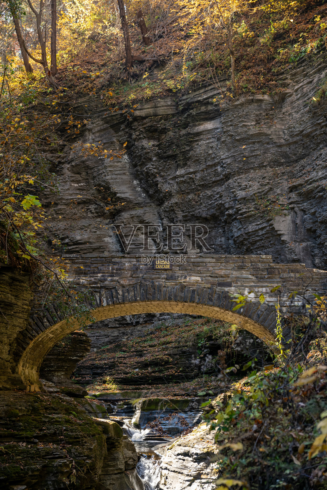 秋季景观：历史悠久的石拱桥坐落在岩石峡谷中，周围环绕着绚丽的秋叶，位于沃特金斯格伦州立公园。照片摄影图片