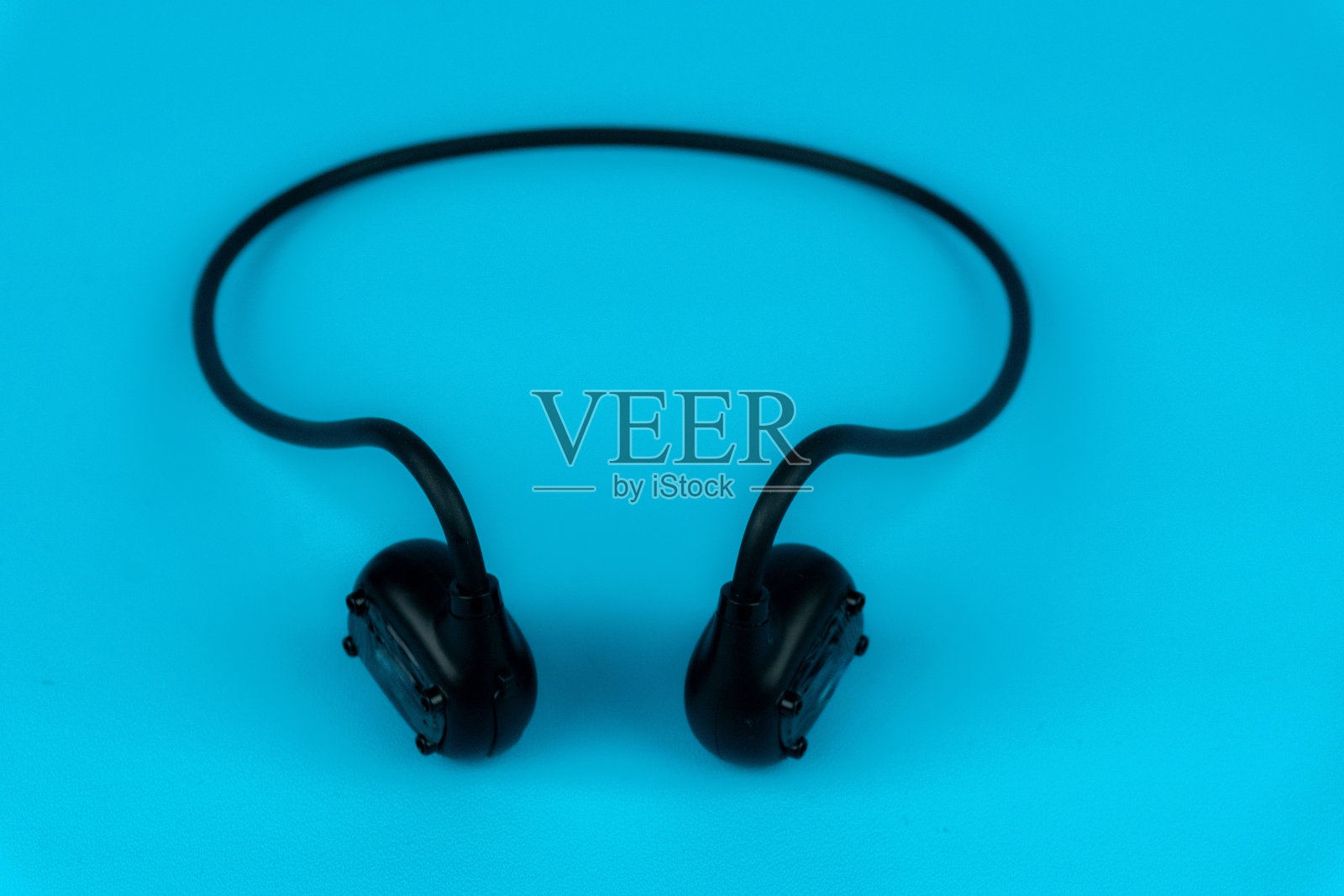一对黑色颈后蓝牙耳机或运动耳机静静地放在蓝色背景上照片摄影图片