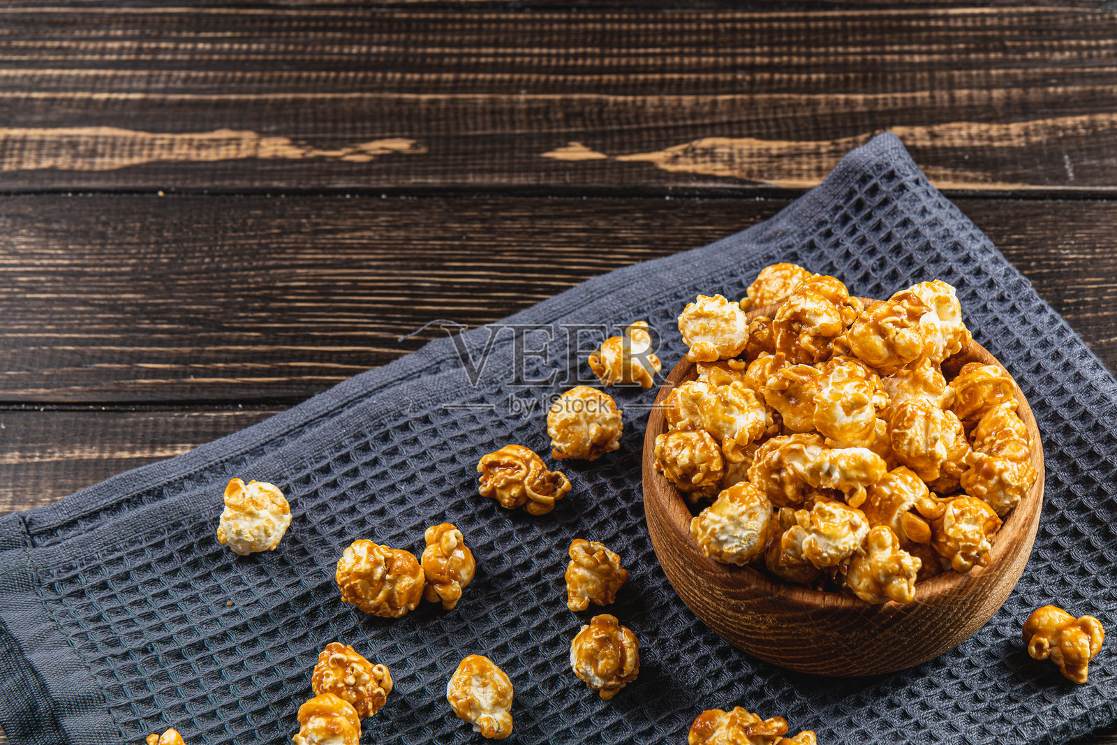 零食概念，碗中盛着甜蜜的焦糖爆米花，背景为灰色木纹。照片摄影图片