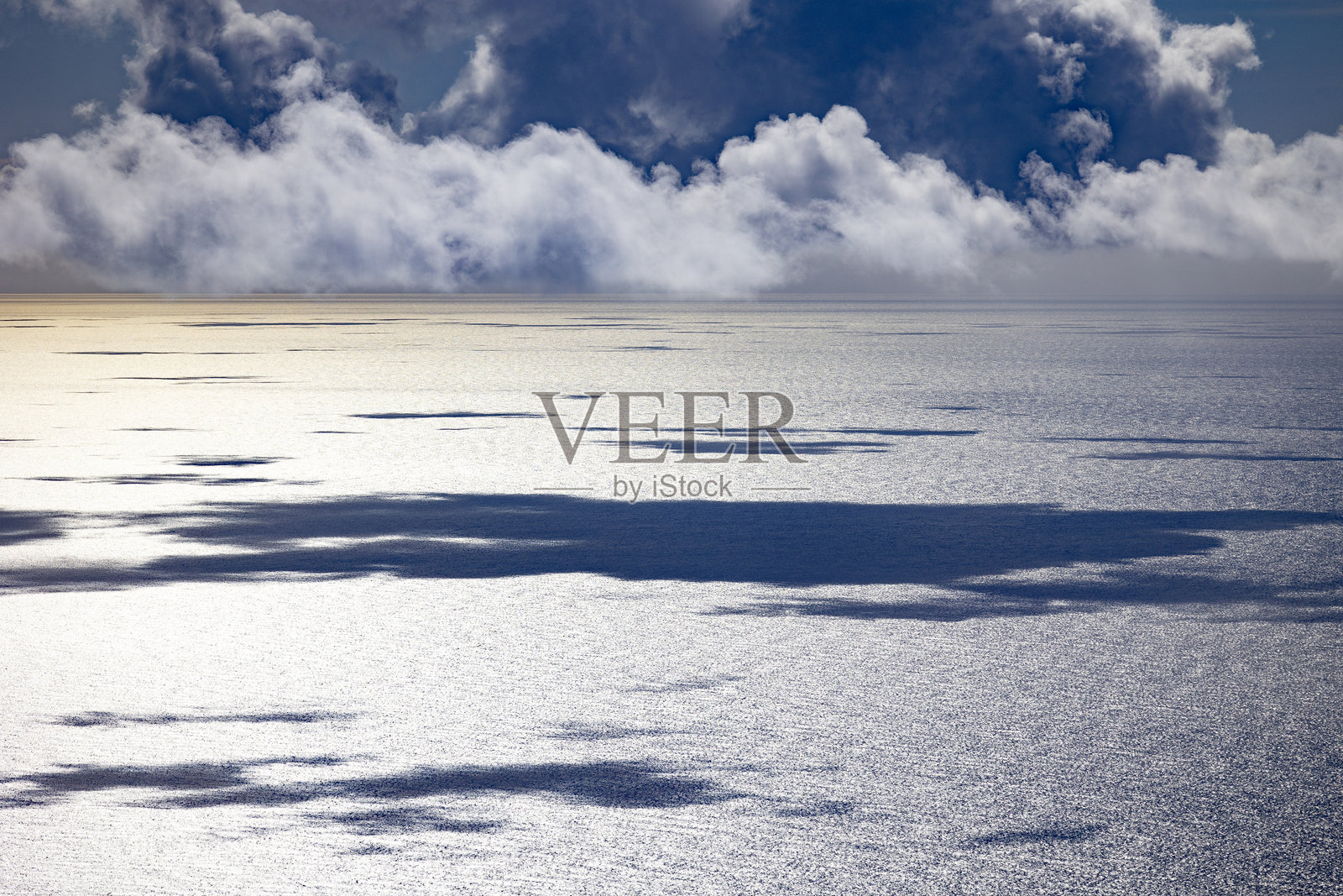 云彩在闪烁的海面上投下柔和的阴影，营造出宁静而富有氛围的海景。照片摄影图片