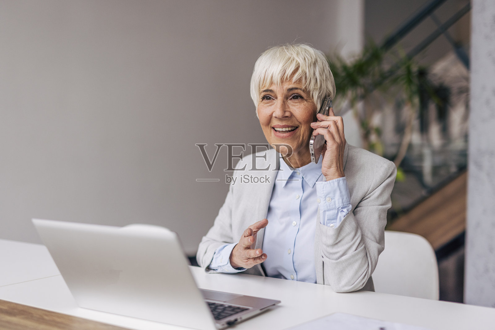 在办公桌前使用手机的资深女商人照片摄影图片