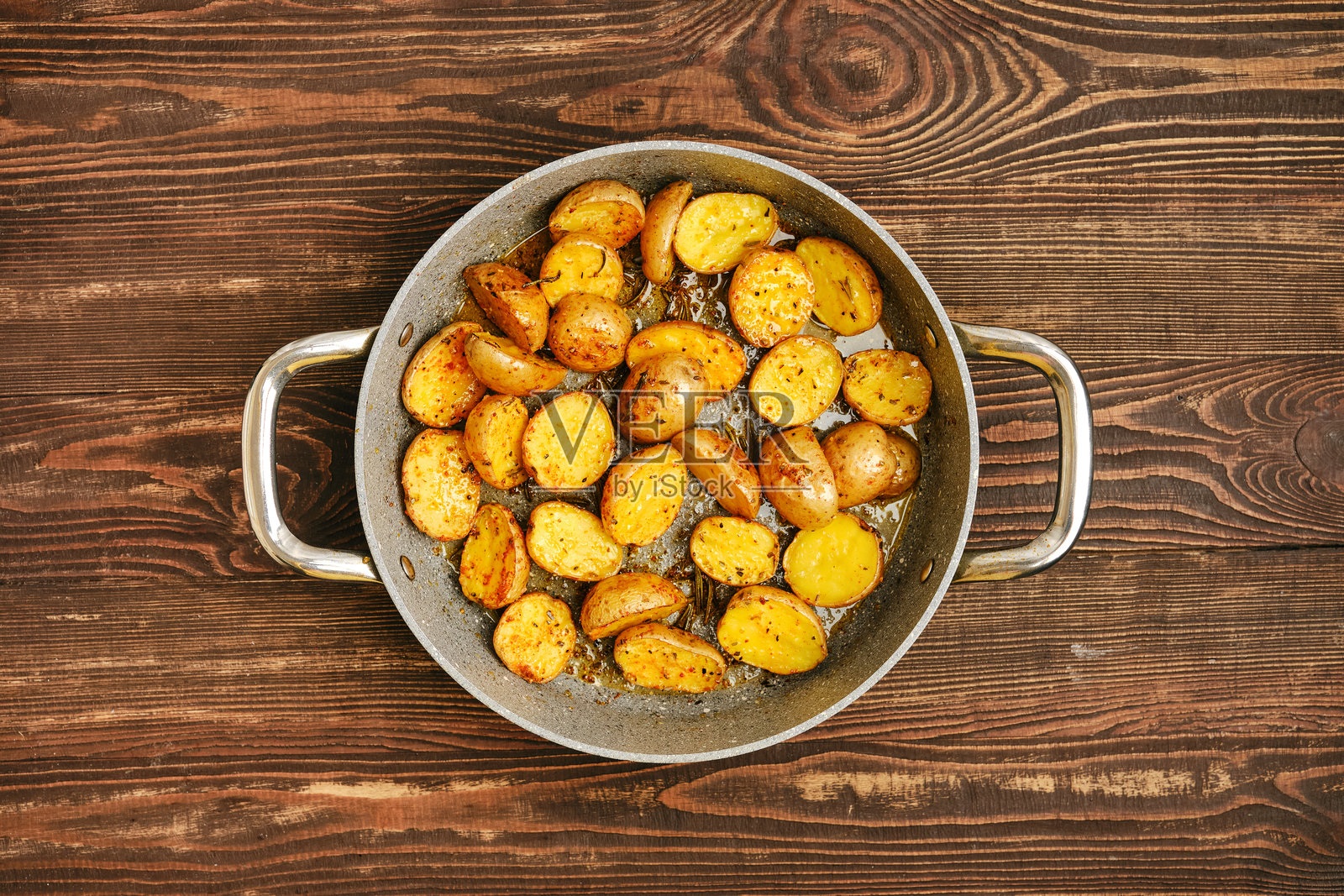 银色平底锅中的酥脆烤土豆，放在木质表面上照片摄影图片