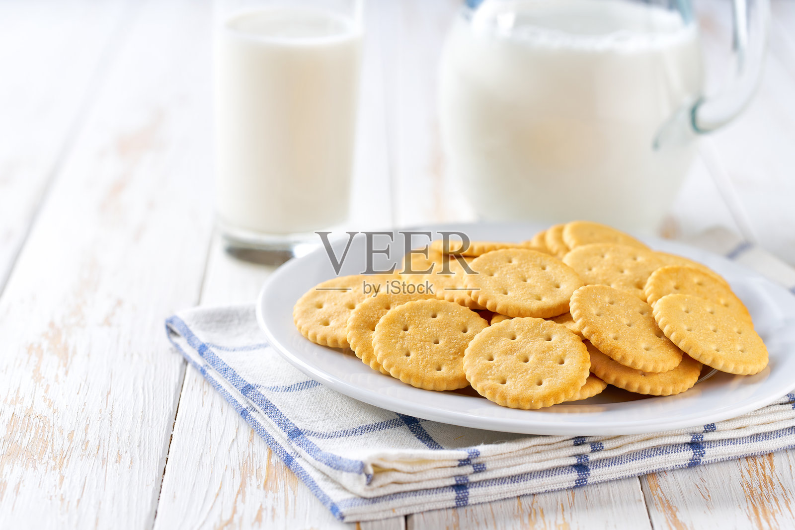 白色桌子上放着一杯新鲜牛奶和一壶牛奶，旁边是圆形的小麦饼干，采用选择性对焦。照片摄影图片