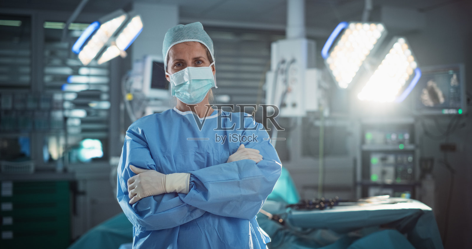 中年女性医生或外科医生佩戴防护口罩、一次性手术帽和工作服的肖像。医疗人员在手术室中平静地看着镜头。照片摄影图片