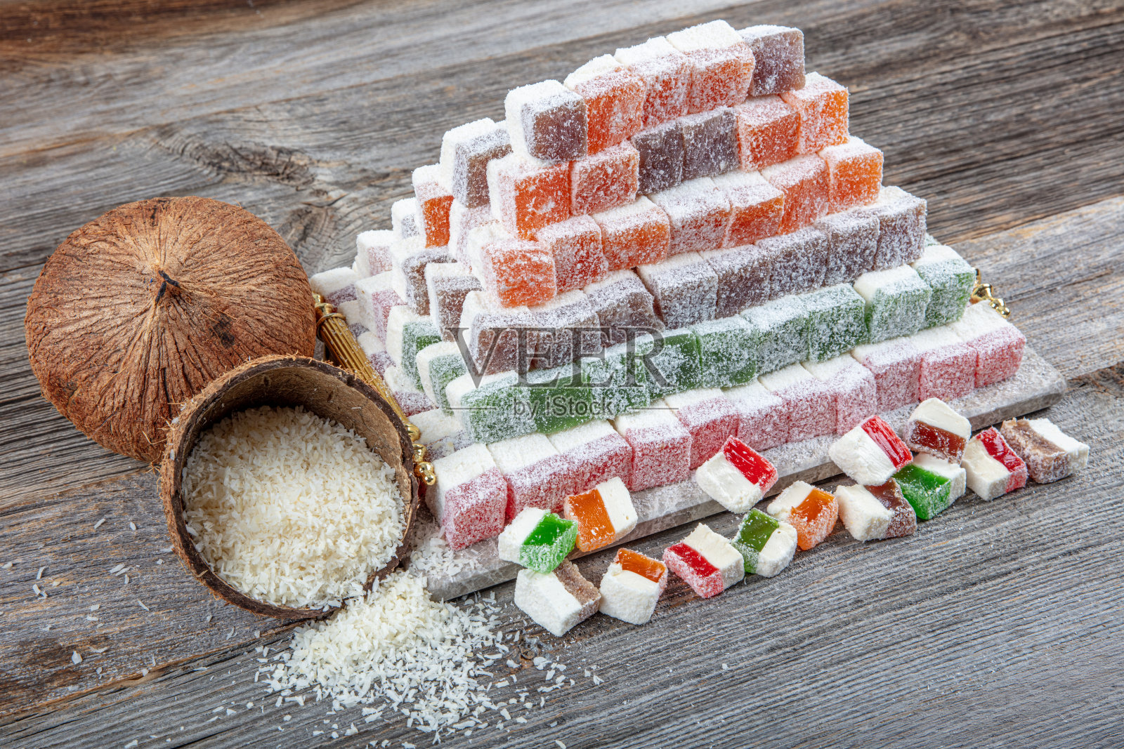 从上方俯视各种不同颜色和口味的土耳其软糖，表面裹有椰子粉，整齐地摆放在大理石托盘上，背景为自然木材。色彩丰富的食品背景，留有空白空间。照片摄影图片