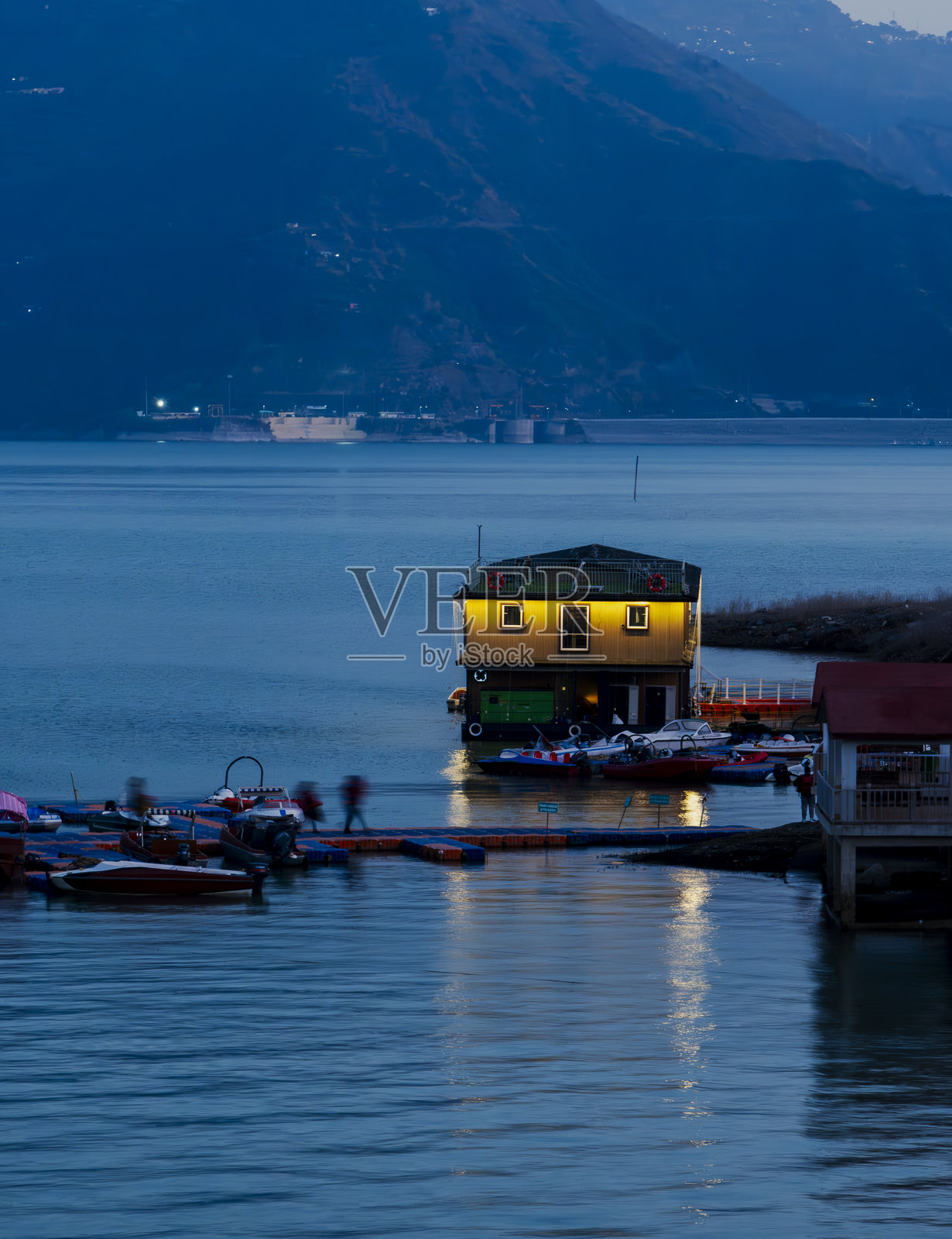 湖面上漂浮着一座灯光闪烁的小屋，蓝色的光芒在水面上美丽地反射，为特赫里湖的风景增添了一丝魔幻的色彩。照片摄影图片