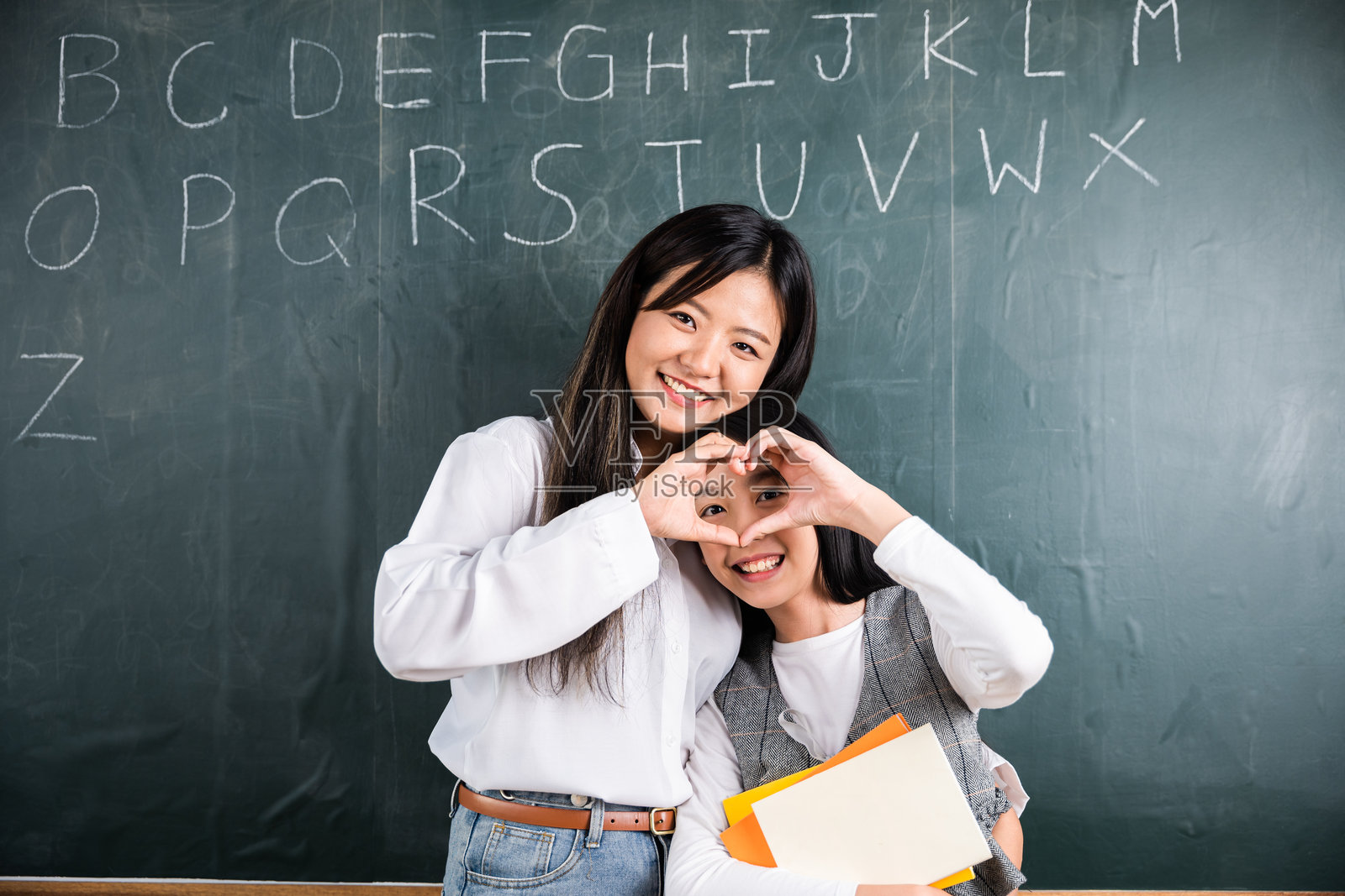 两位女性手牵手在黑板上做出一个心形。照片摄影图片