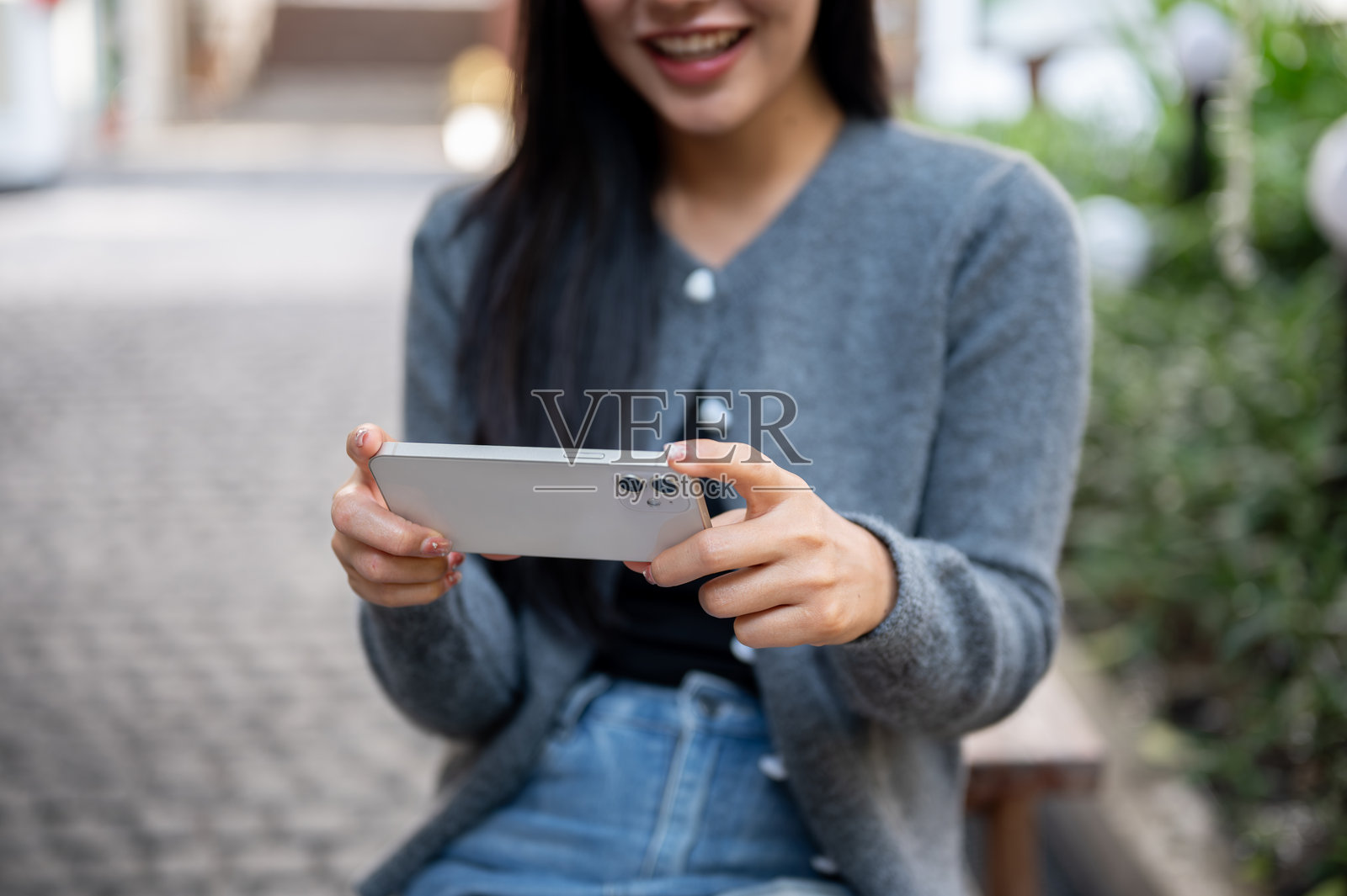 一位快乐的亚洲女性坐在户外长椅上，近距离使用她的智能手机。照片摄影图片