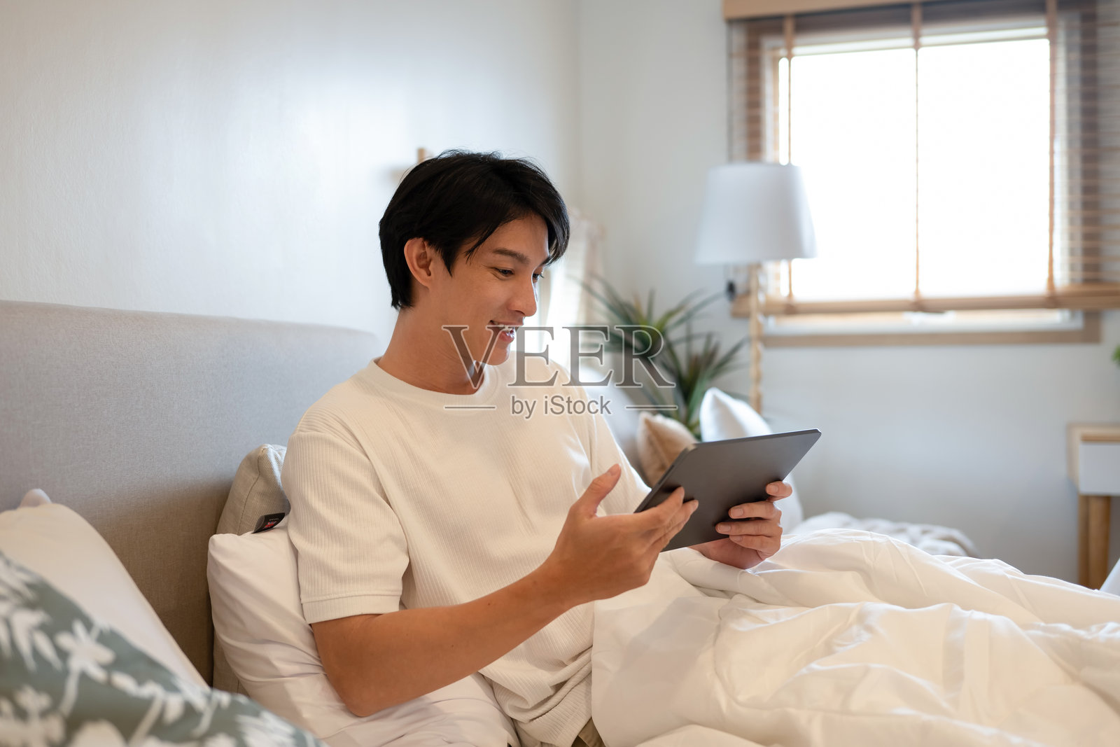 快乐的亚洲成年人在卧室里用平板电脑上网照片摄影图片