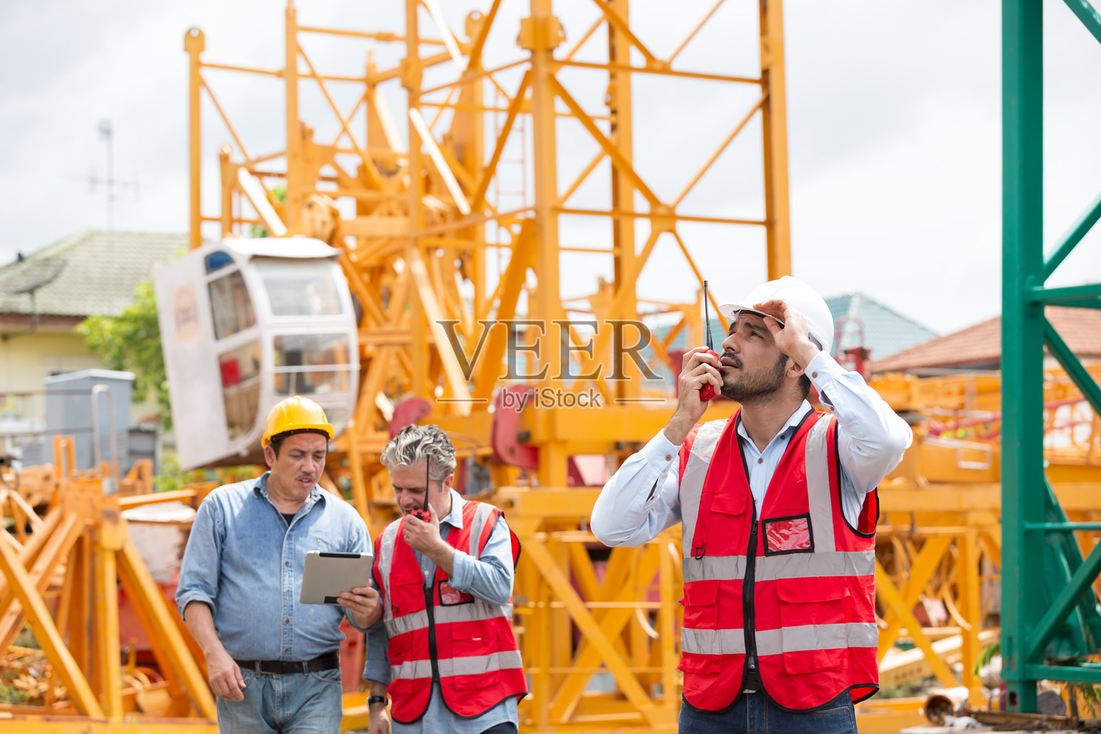 男性工程师在建筑工地上使用对讲机检查和控制工作，背景中是一组工程师团队正在工作。照片摄影图片
