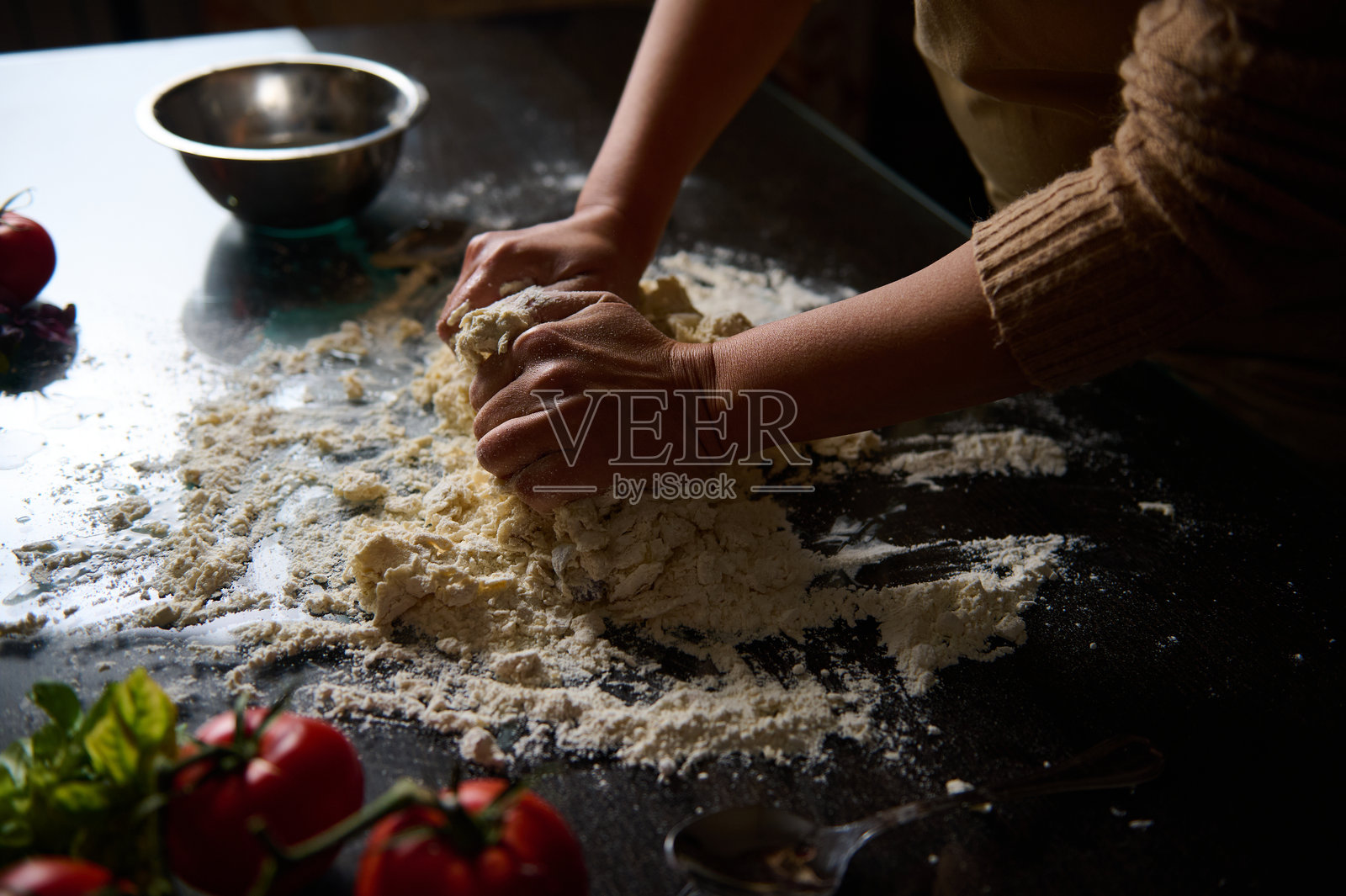 双手在撒了面粉的桌面上揉面团，旁边有新鲜的食材。照片摄影图片